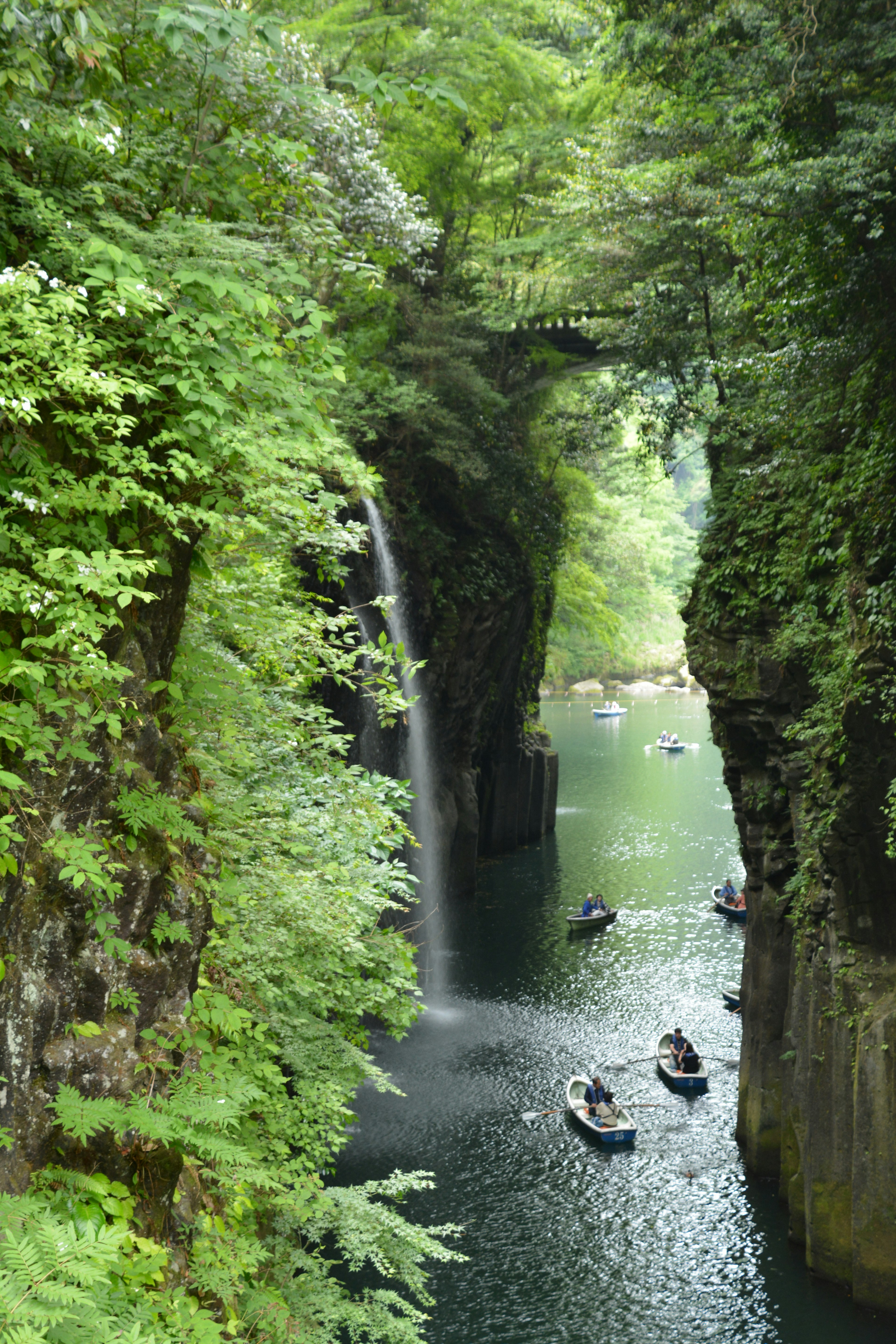 A scenic view of a green canyon with small boats on a river and a waterfall