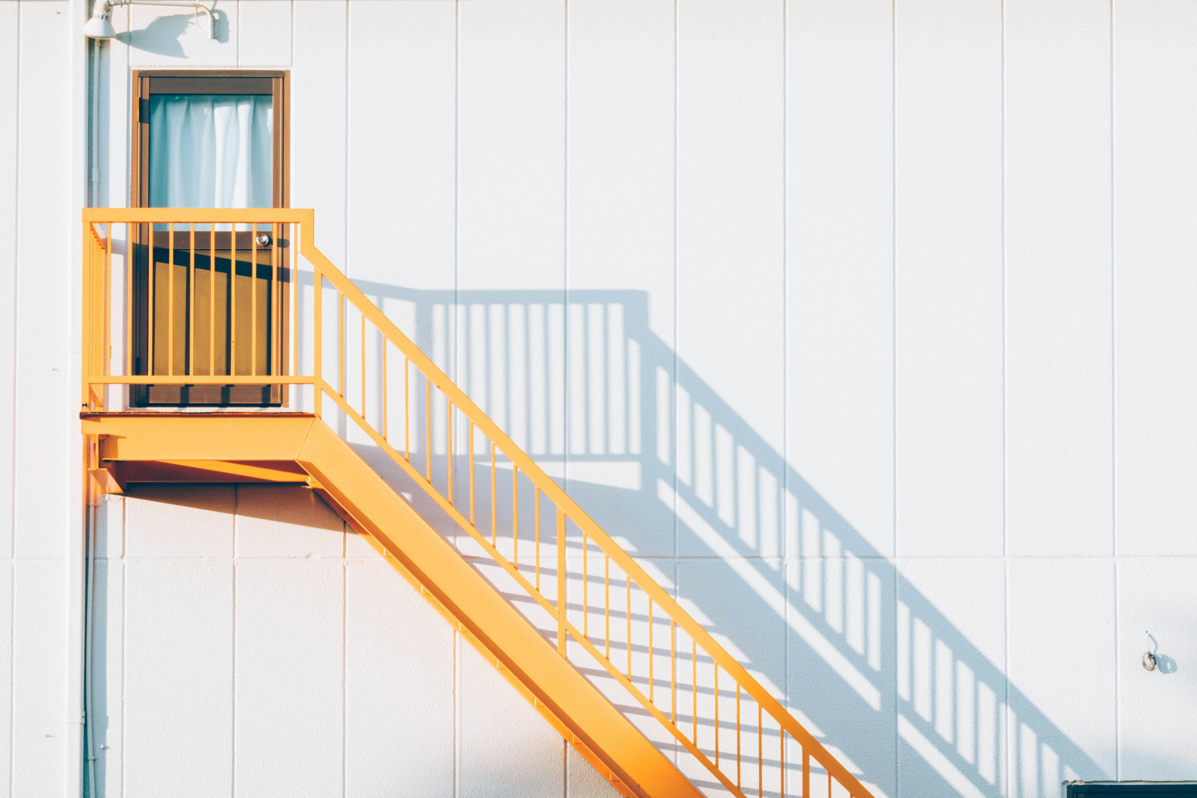 Vista exterior de un edificio con una escalera naranja contra una pared blanca