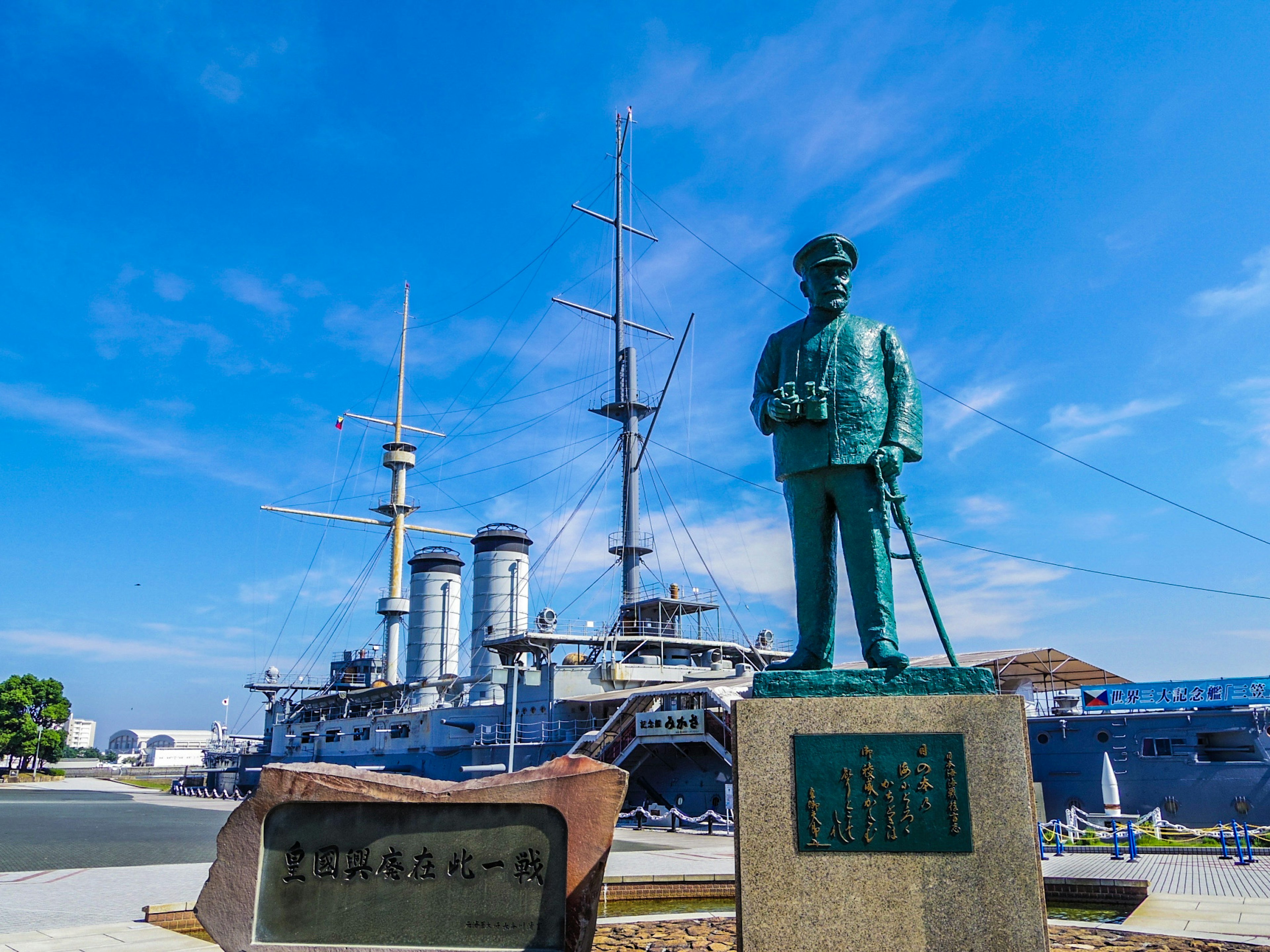 Statue of a military figure under a blue sky with a battleship in the background