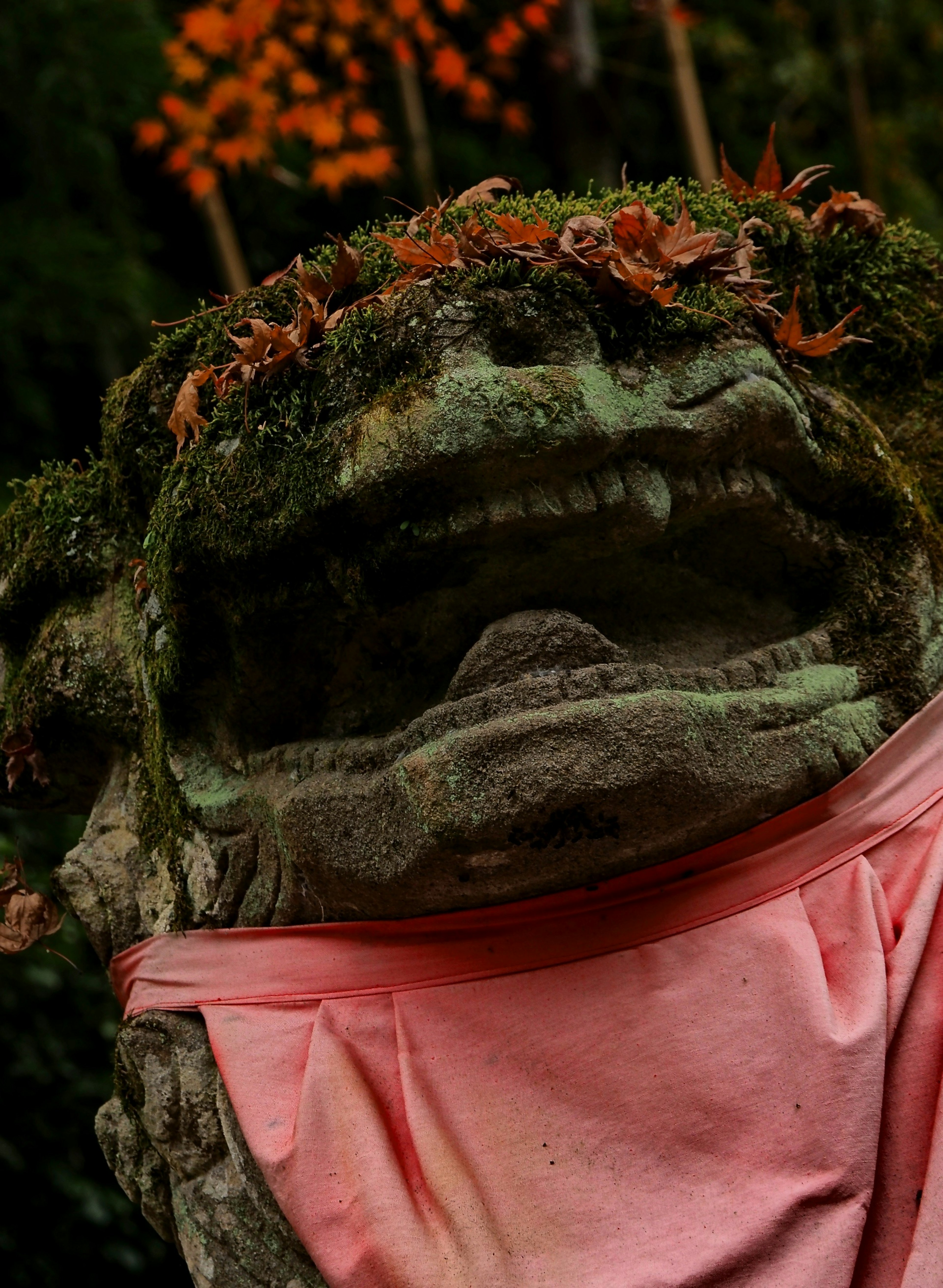 Estatua de piedra cubierta de musgo verde con una tela rosa