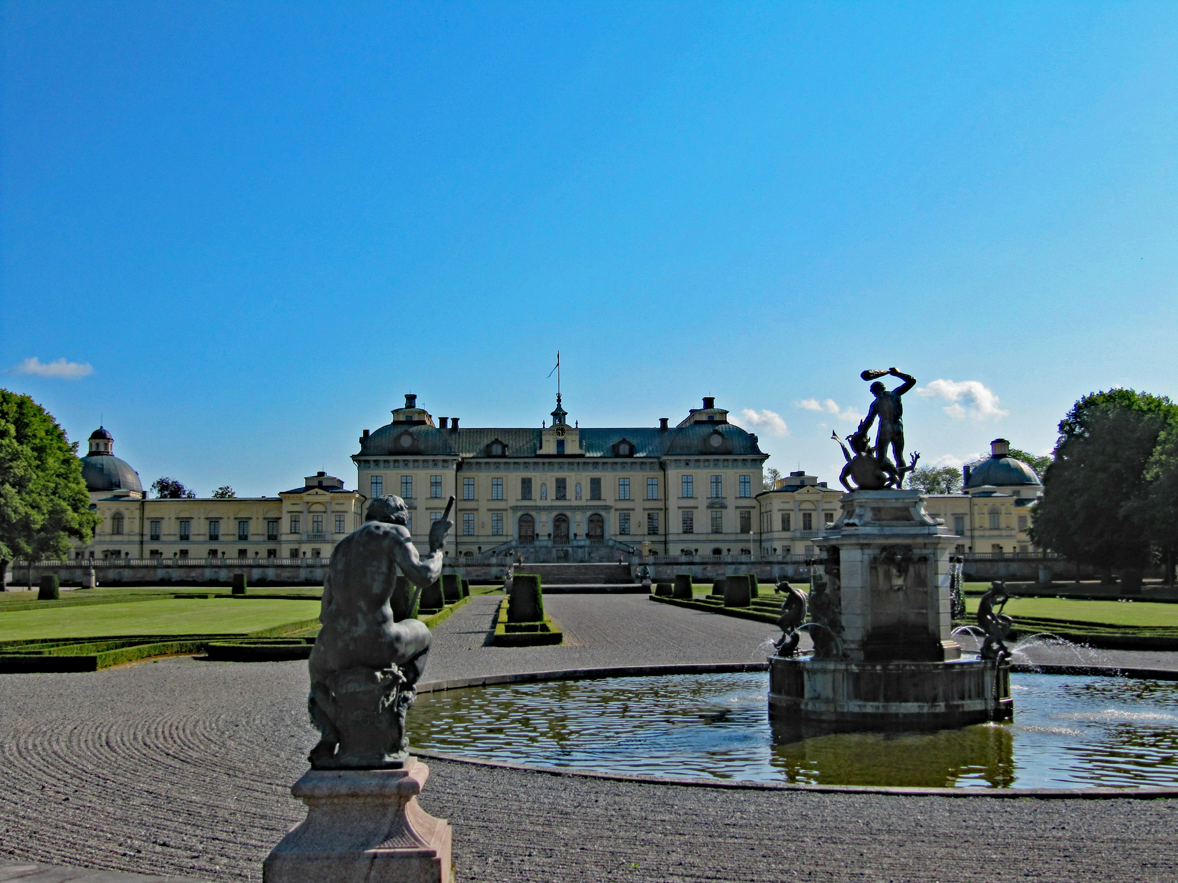 Großer Palast umgeben von schönen Gärten mit Statuen und einem Brunnen