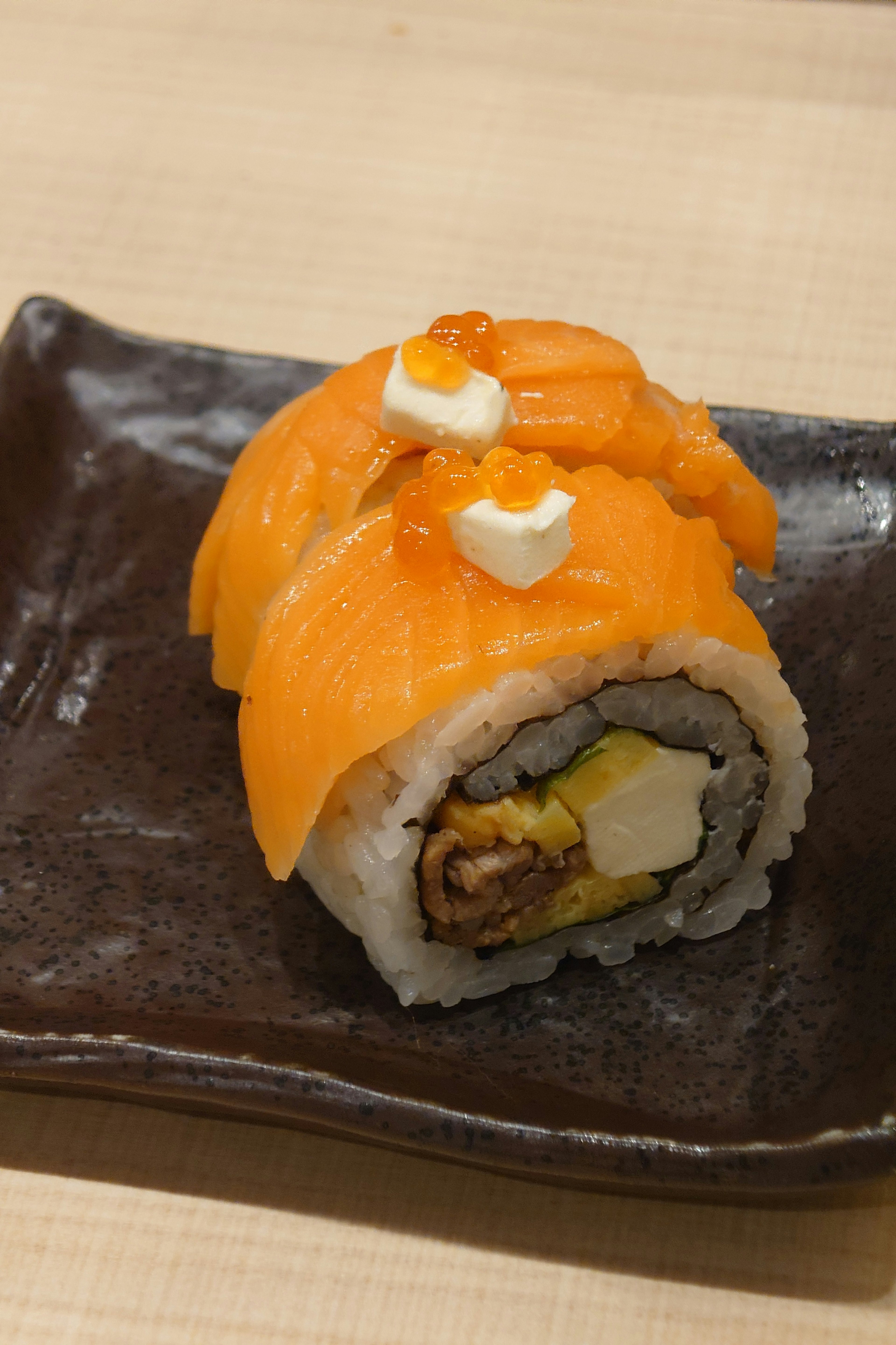 Rollo de sushi naranja vibrante en un plato negro