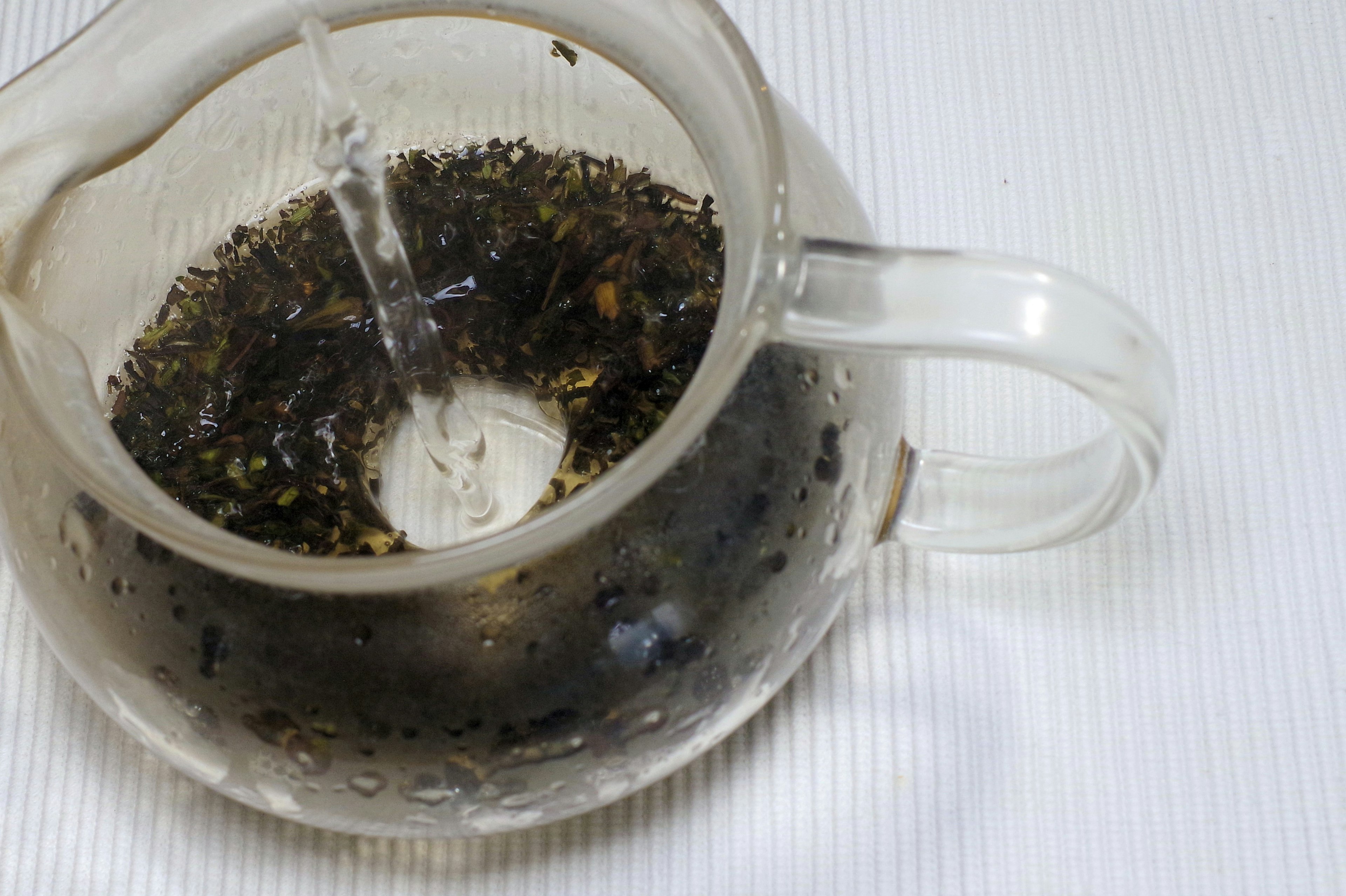 A clear teapot with tea leaves steeping in dark liquid