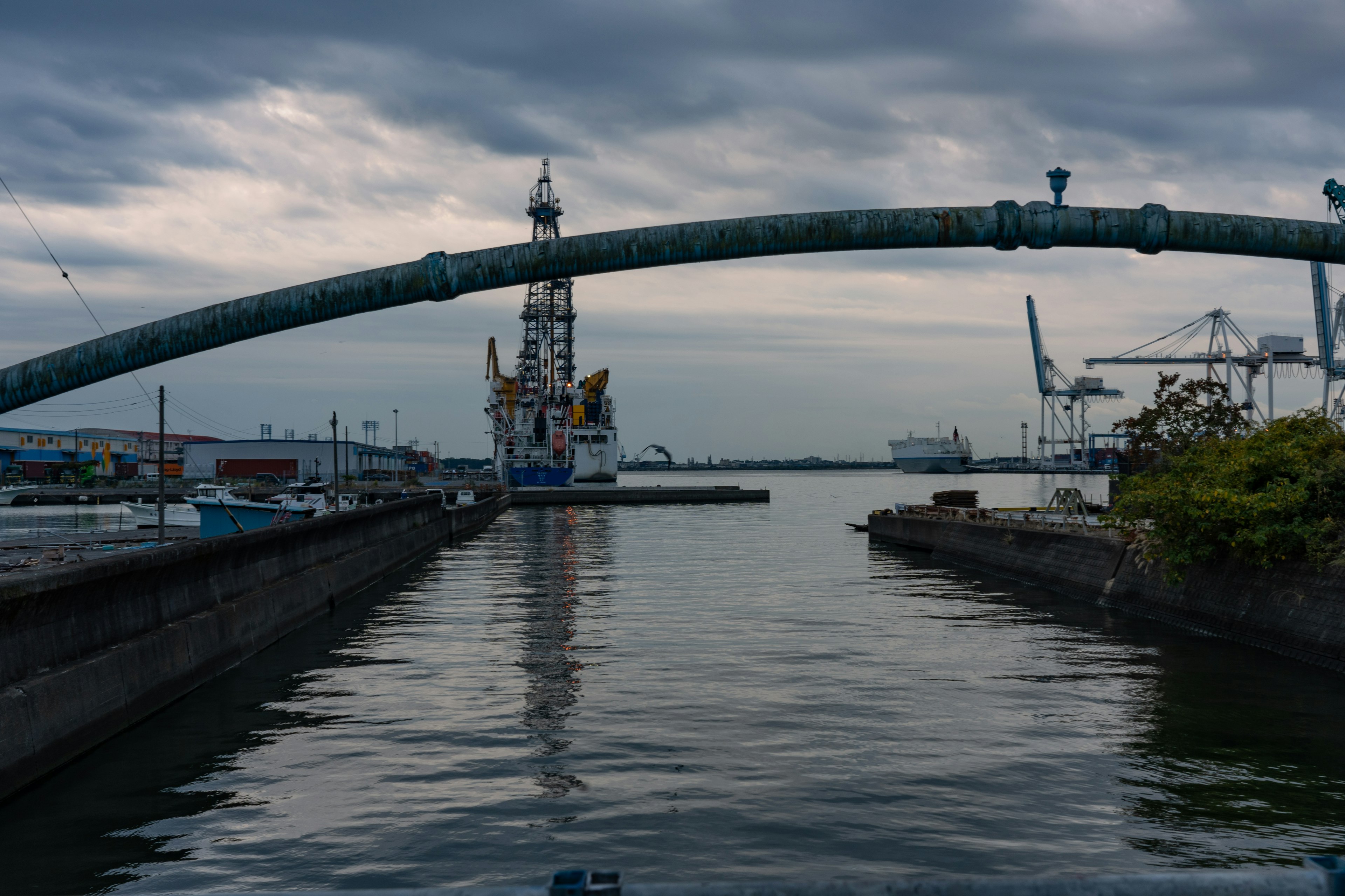 Industrial landscape along a harbor waterway featuring large cranes and a ship