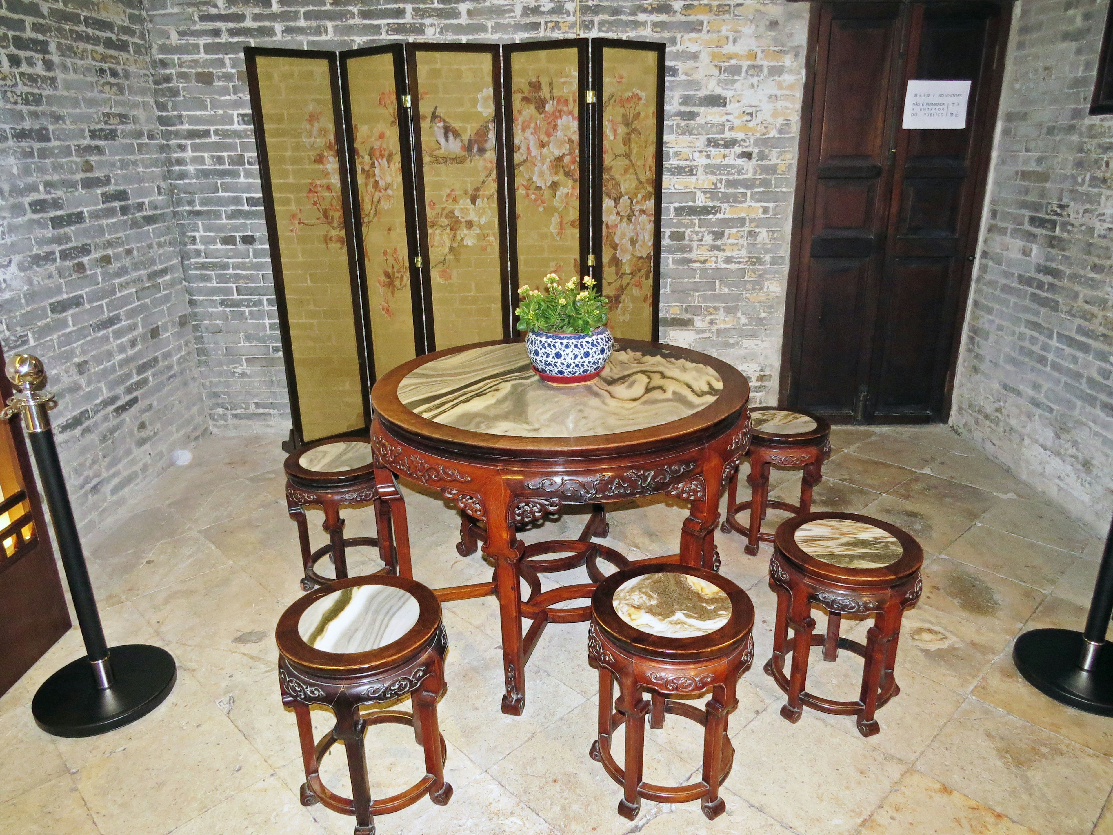 Interior con una mesa redonda de madera y taburetes con una planta decorativa y una pantalla plegable