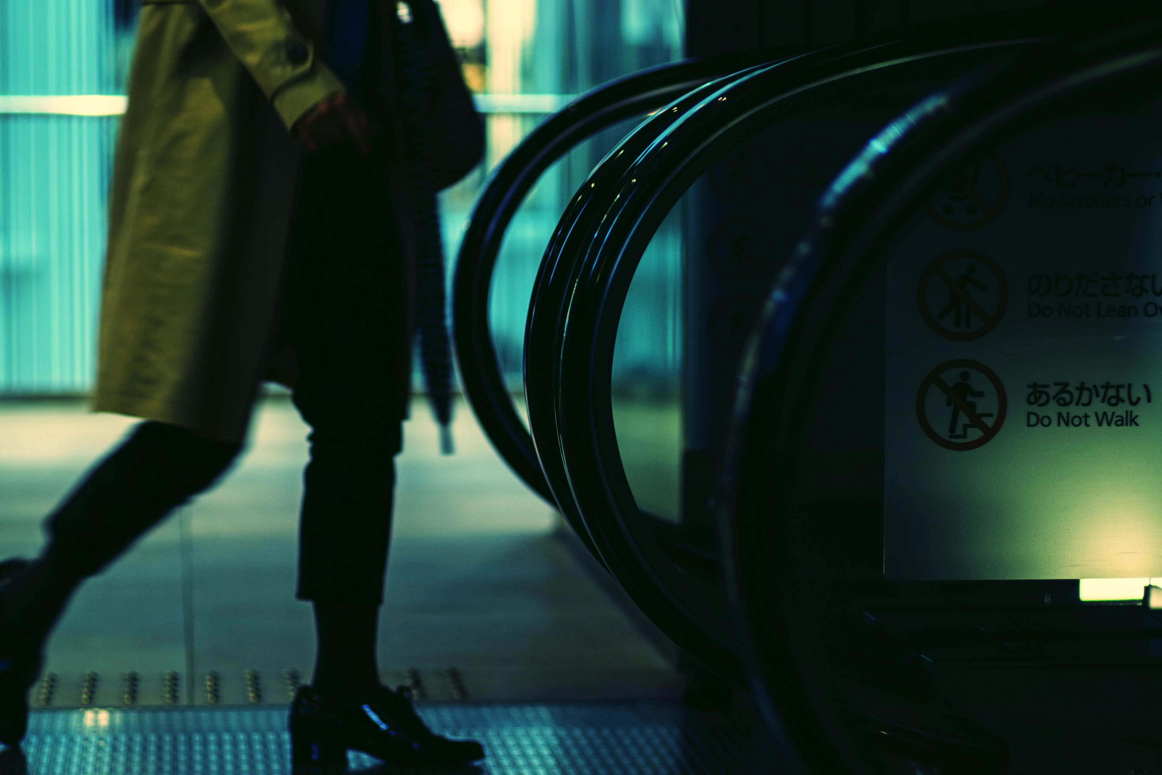 Silueta de una persona caminando cerca de una escalera mecánica débilmente iluminada con pasamanos