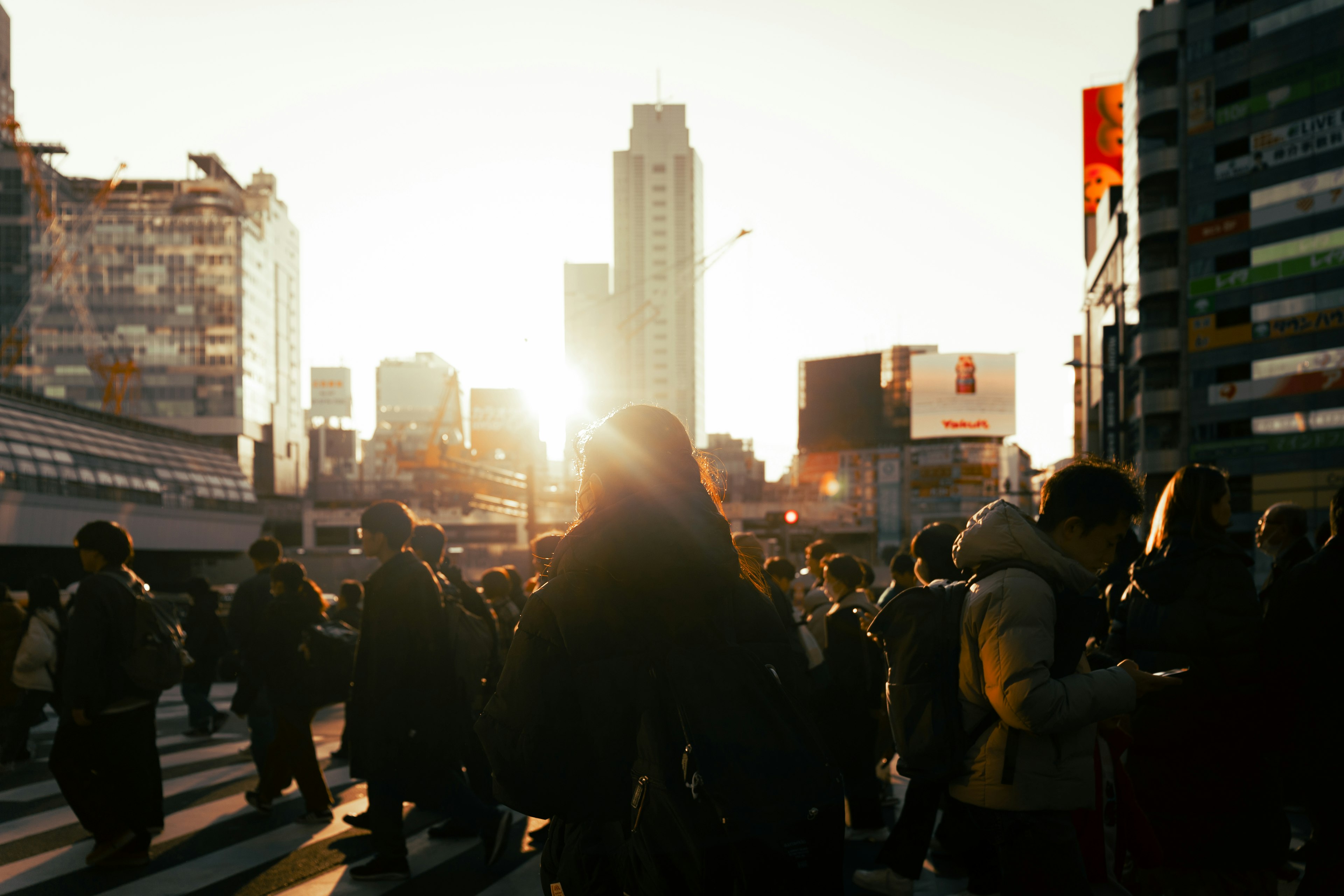 夕日を背景にした都市の交差点で多くの人々が行き交う風景