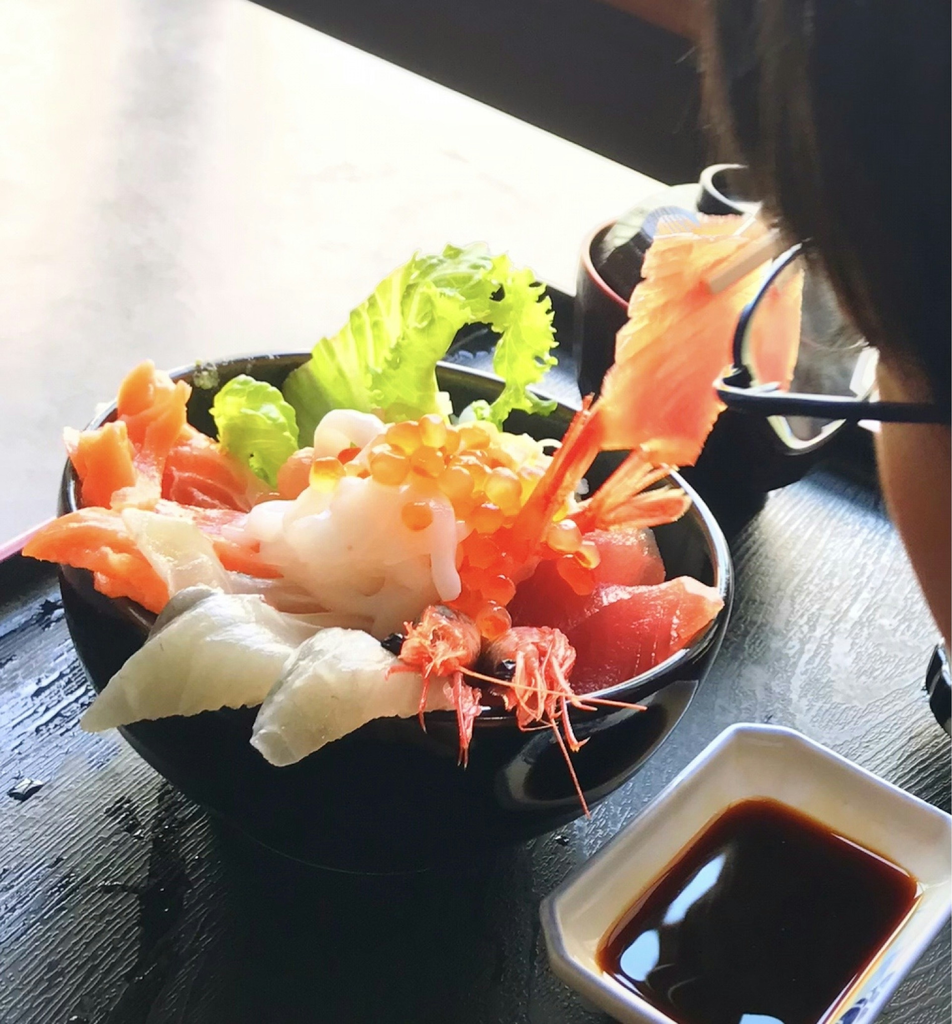 Un tazón de sashimi fresco y camarones adornado con lechuga