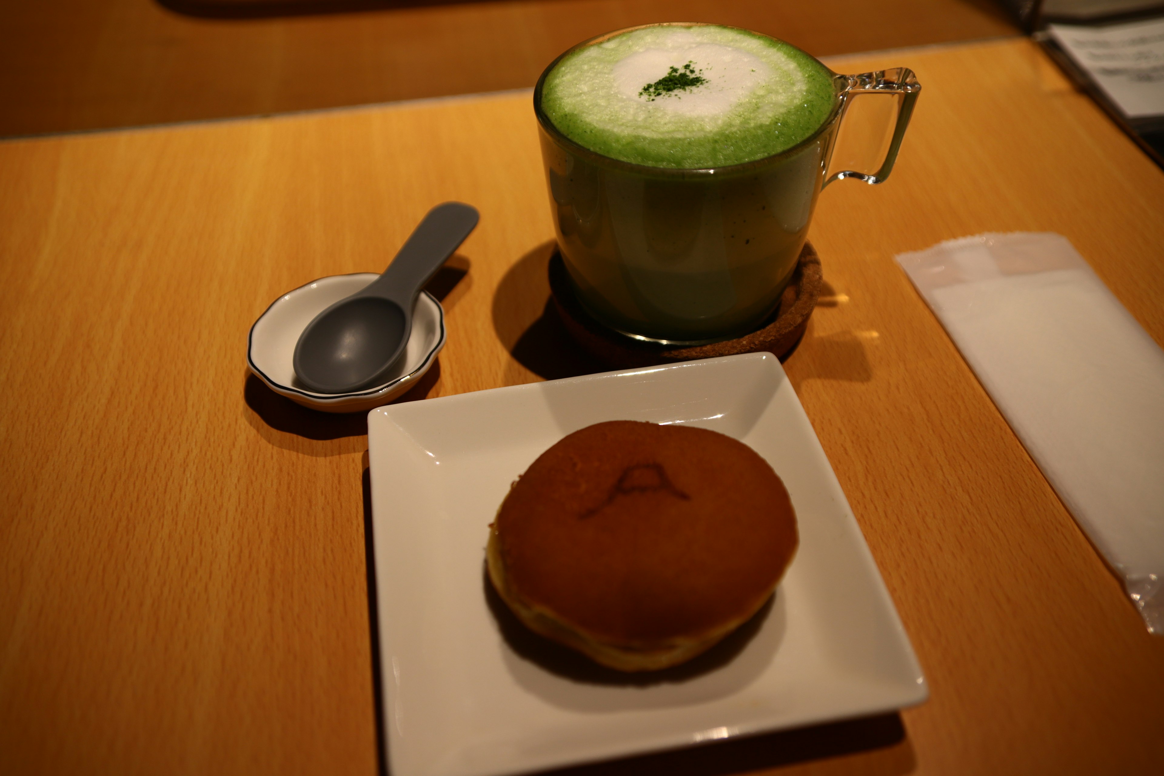 Ein Matcha-Latte und ein japanisches Süßgebäck auf einem Teller auf einem Holztisch