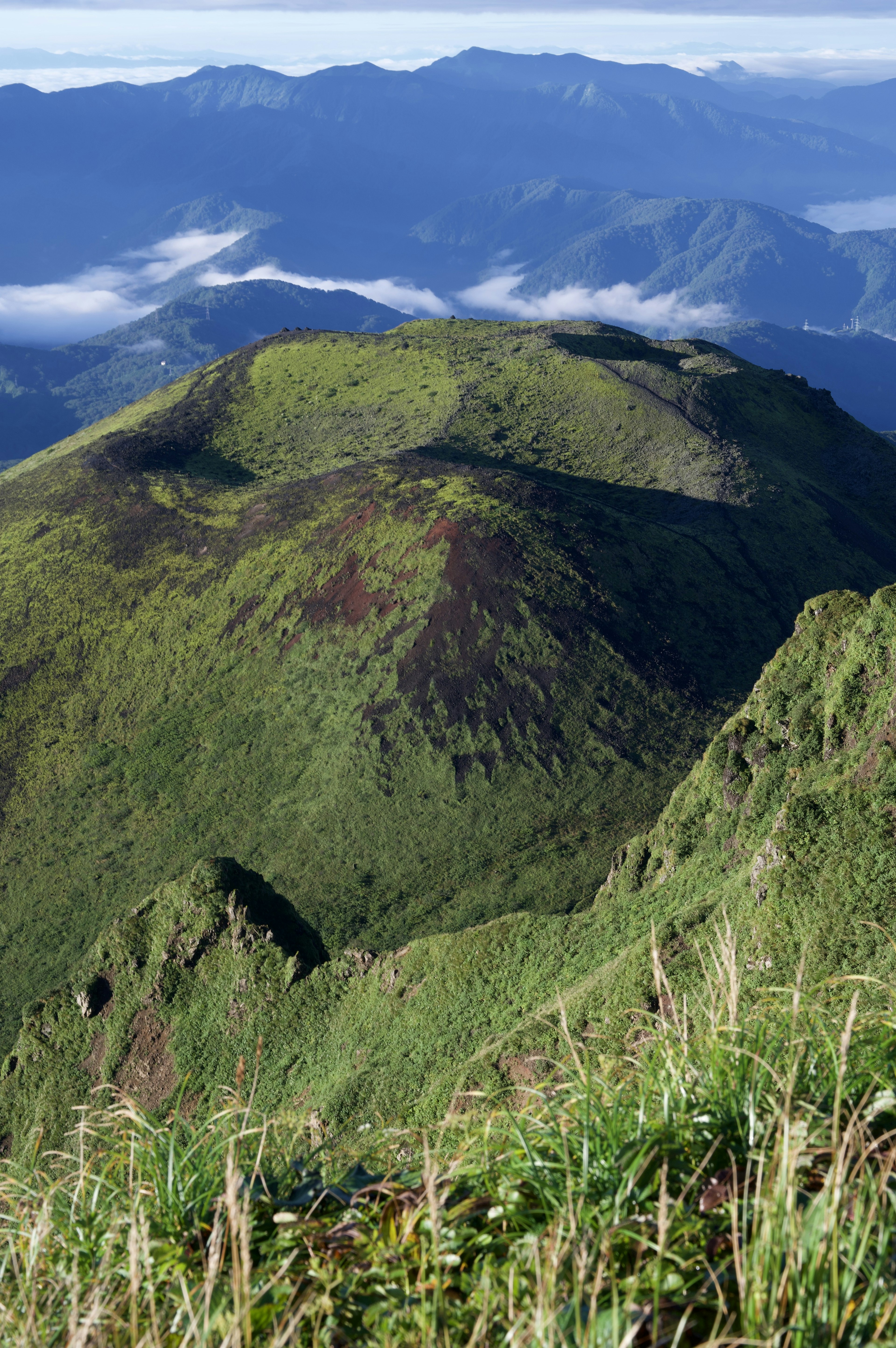 Üppige grüne Berglandschaft mit entferntem Gebirgszug