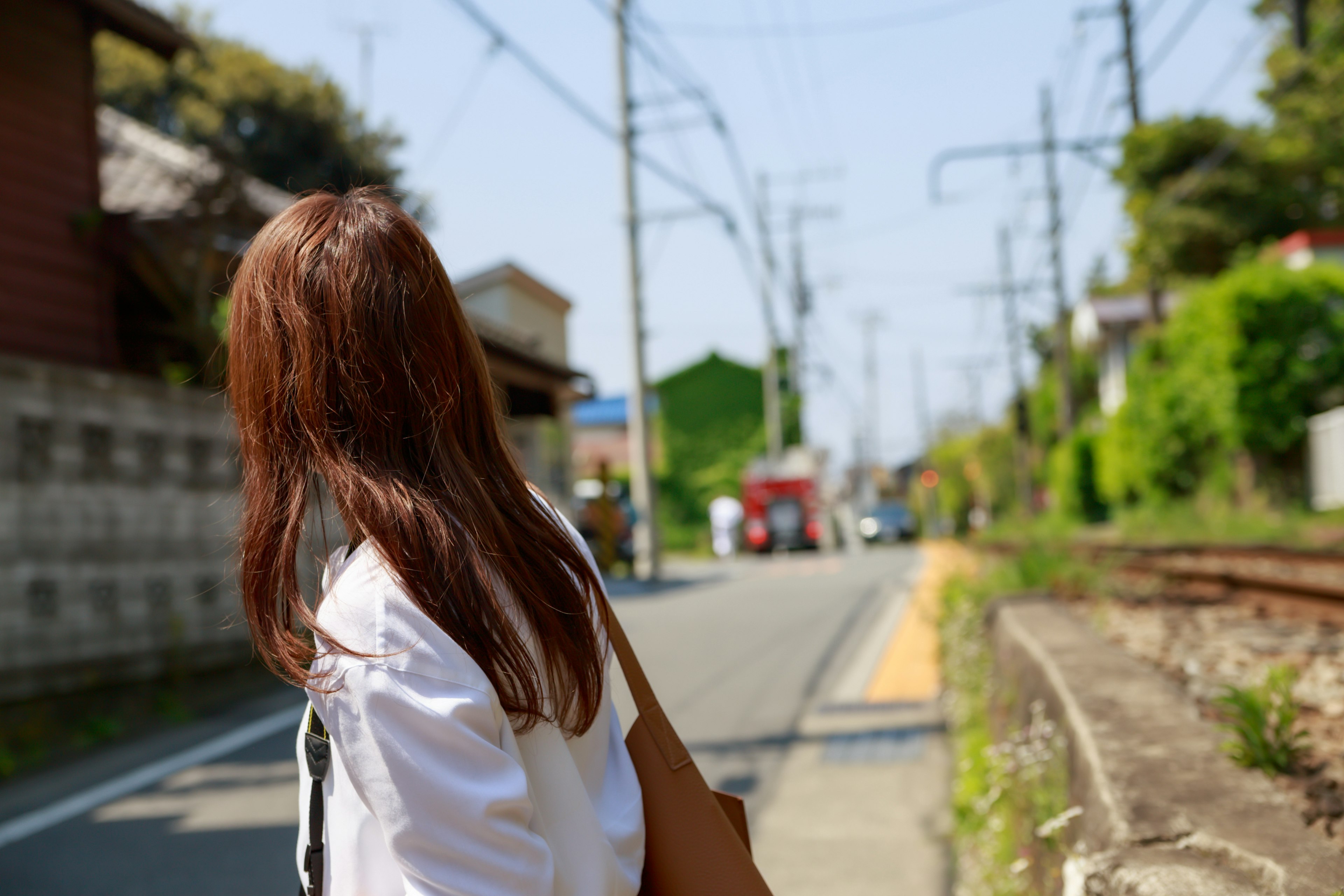 Mujer mirando hacia atrás en una escena de calle con rieles y postes eléctricos visibles