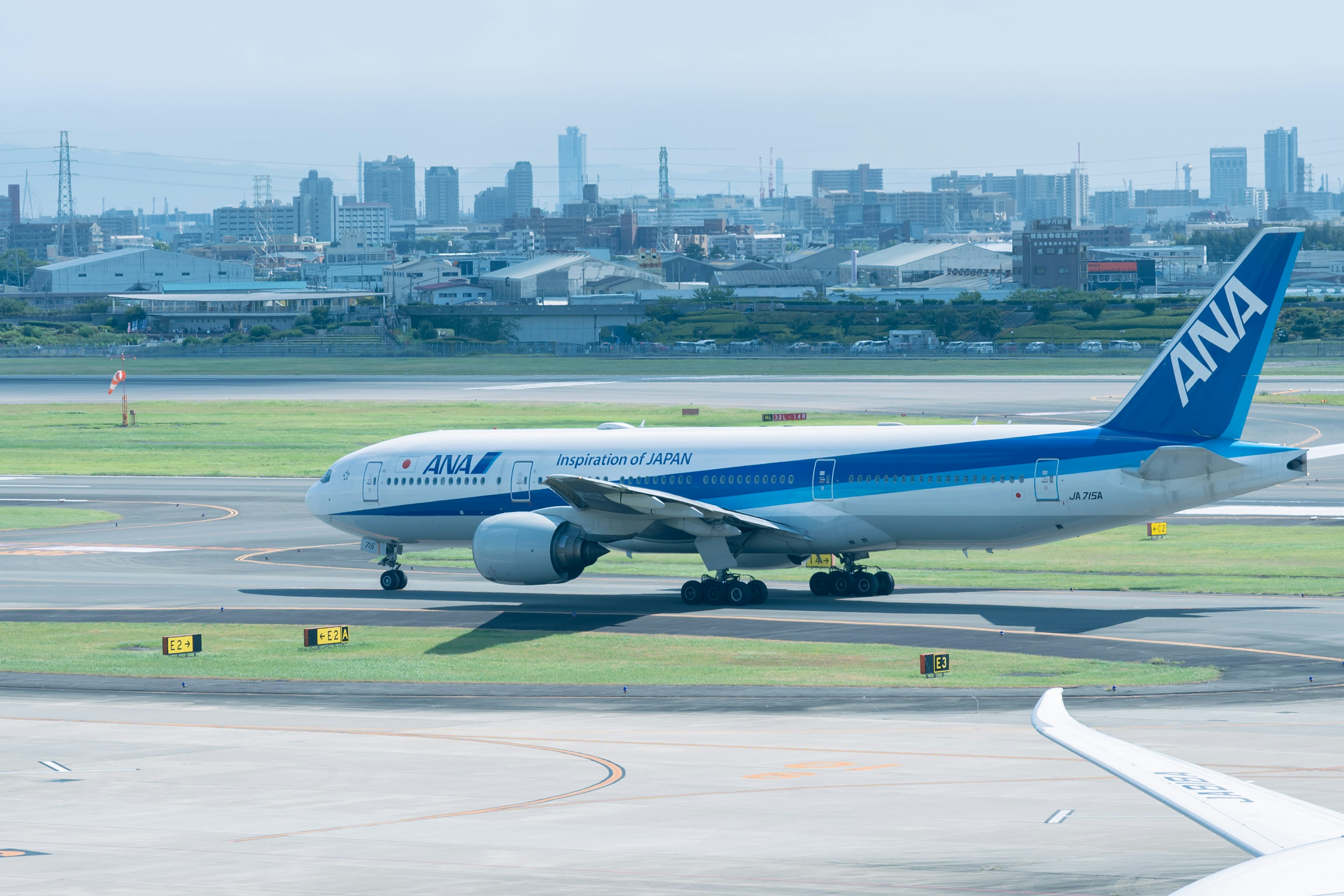 ANA airplane taxiing on runway with city skyline in background