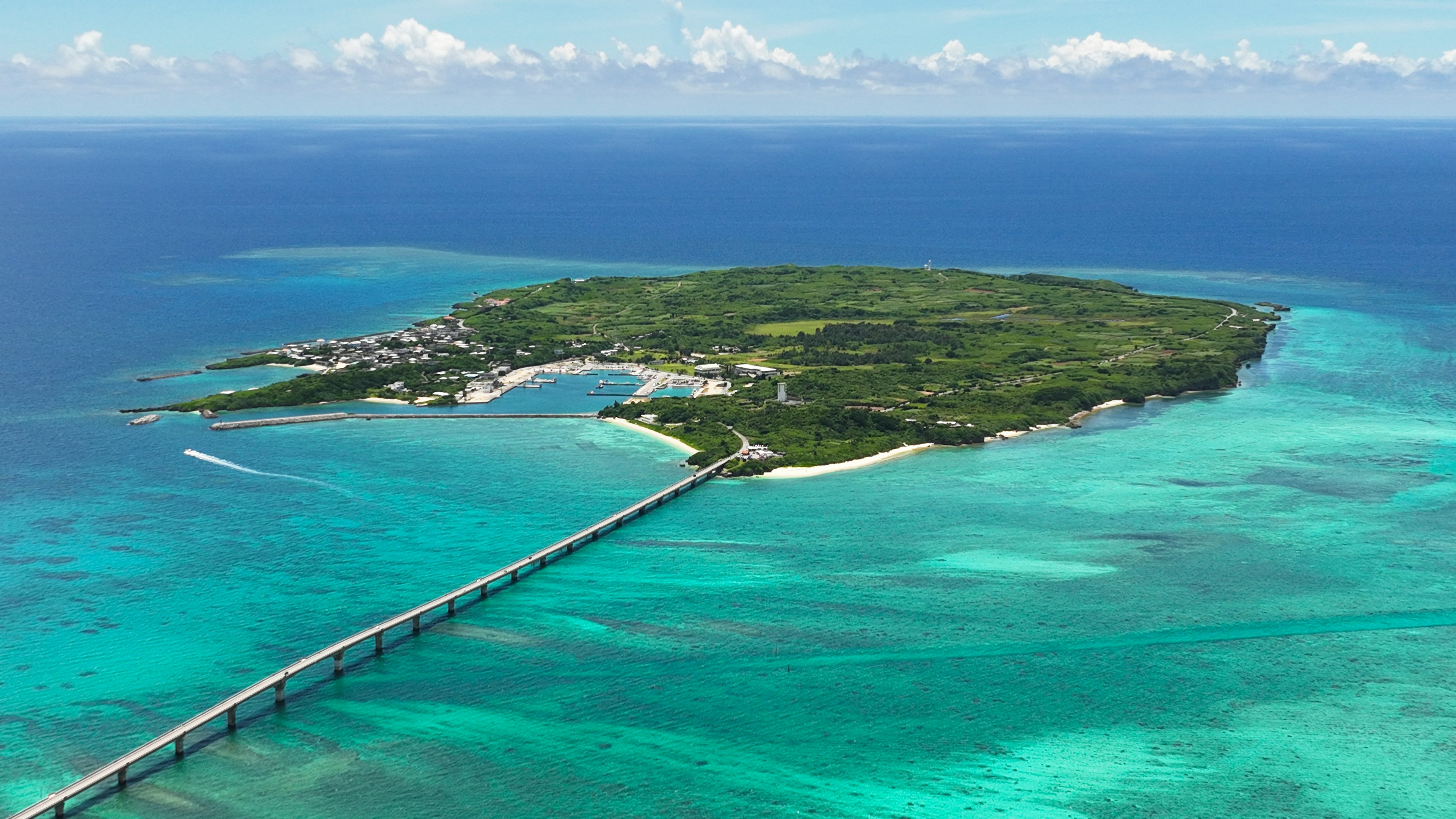 Pemandangan udara pulau hijau yang dikelilingi lautan biru dengan jembatan menghubungkan ke daratan