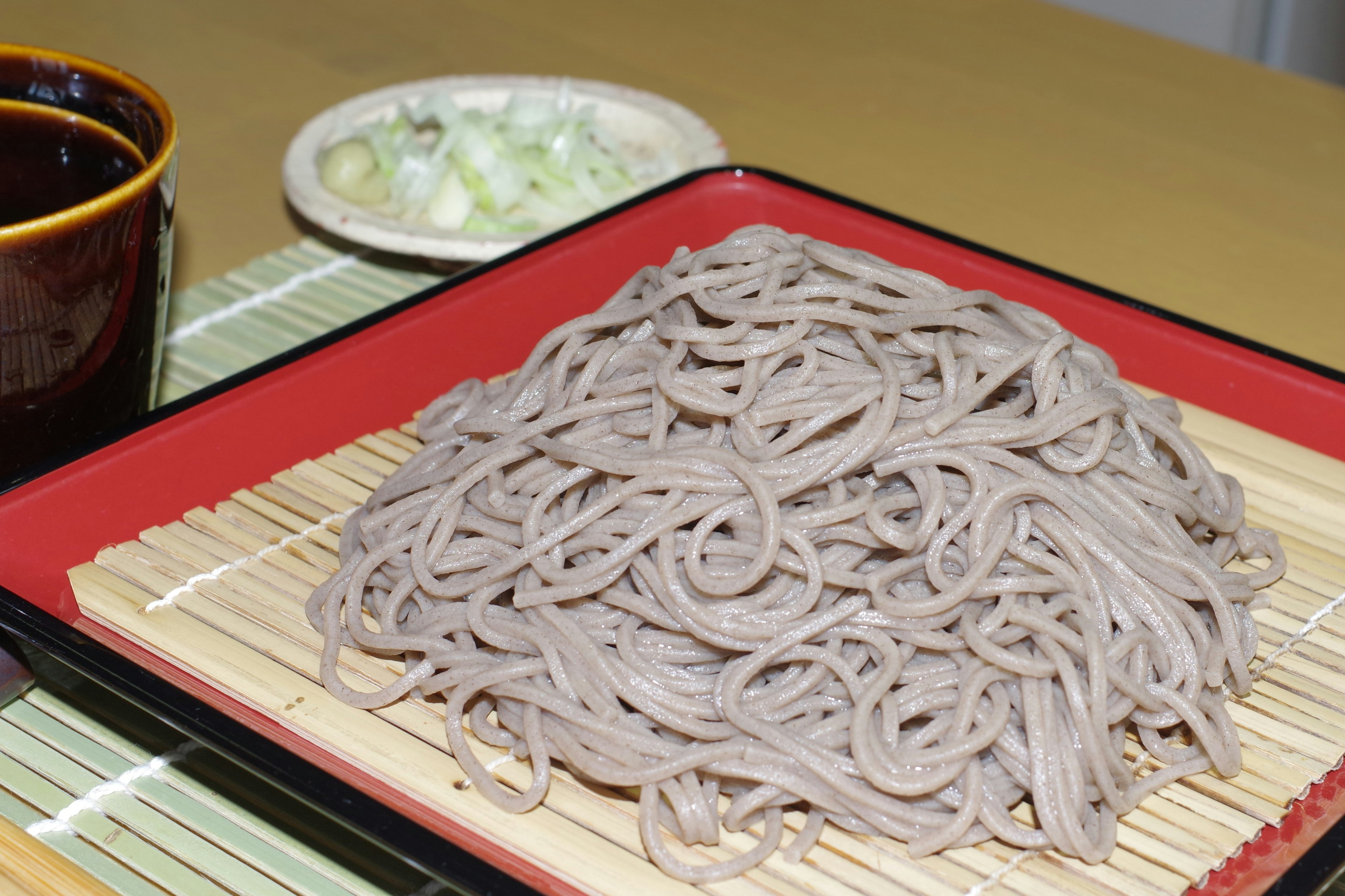 Soba servie sur une assiette rouge avec de la sauce et des oignons verts hachés