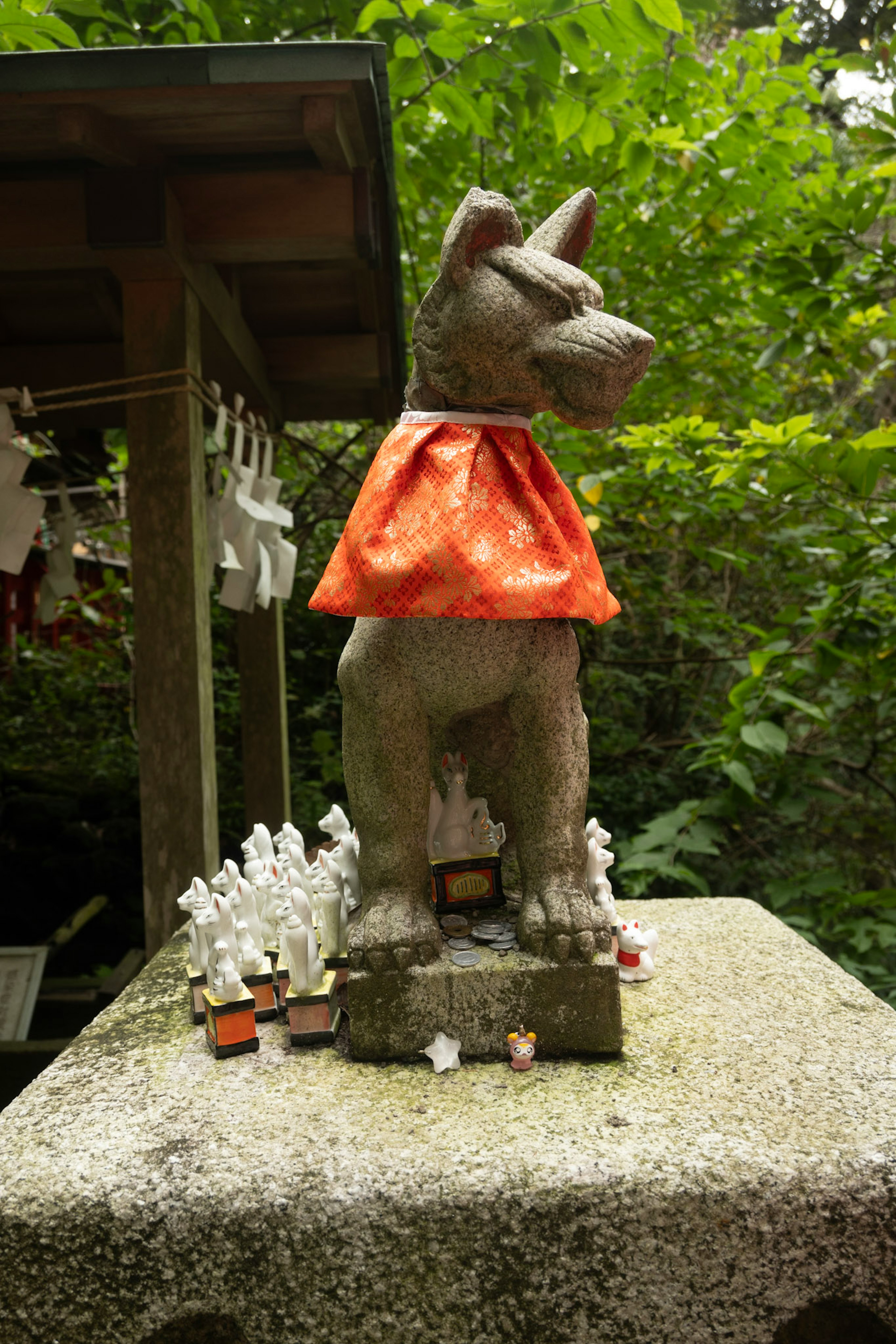 Statua di cane in pietra con un mantello arancione circondata da piccole figurine