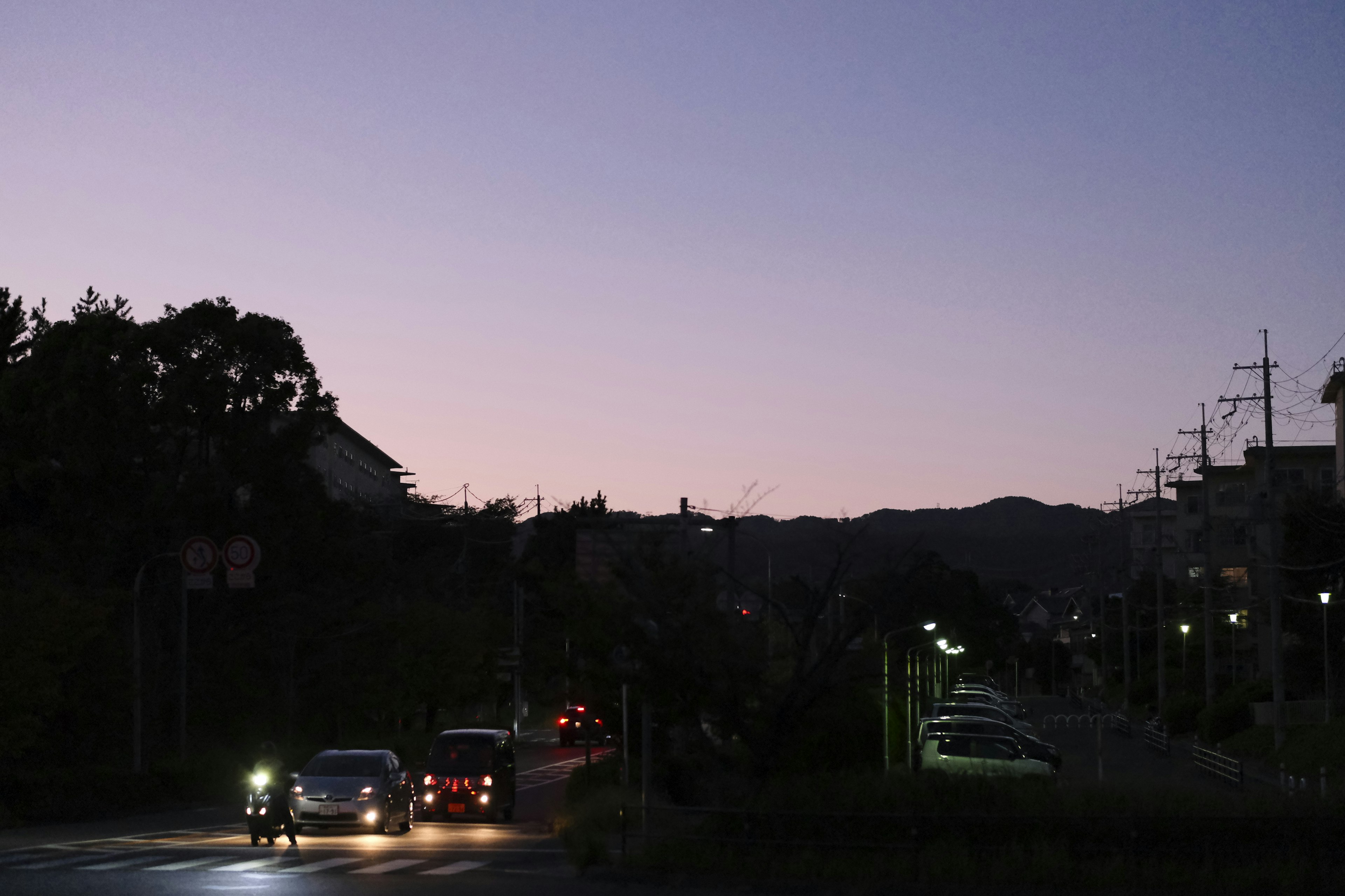 Voitures sur une route au crépuscule avec silhouettes de collines