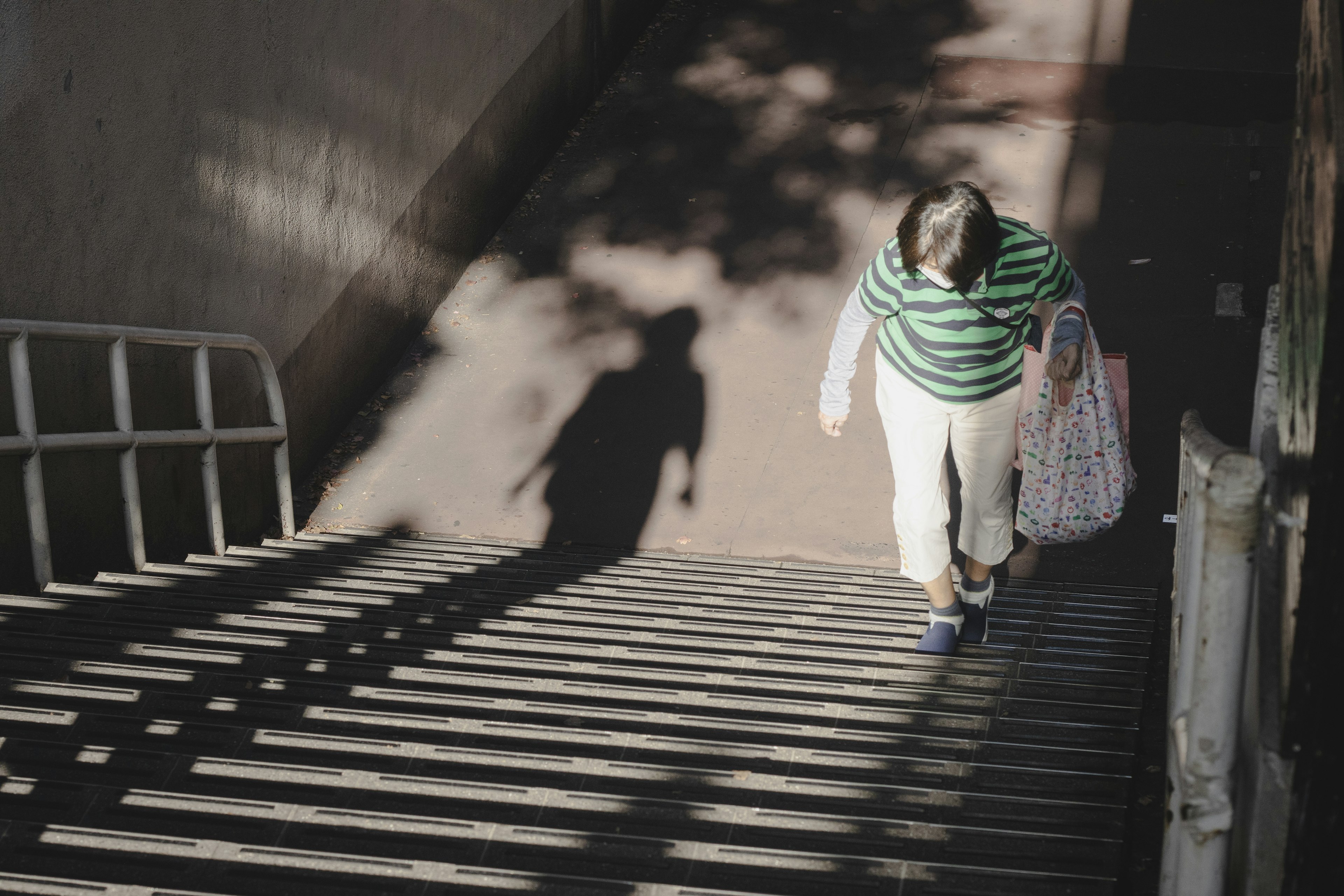 Mujer bajando escaleras vestida con una camiseta de rayas verdes y pantalones blancos con sombras proyectadas por la luz del sol