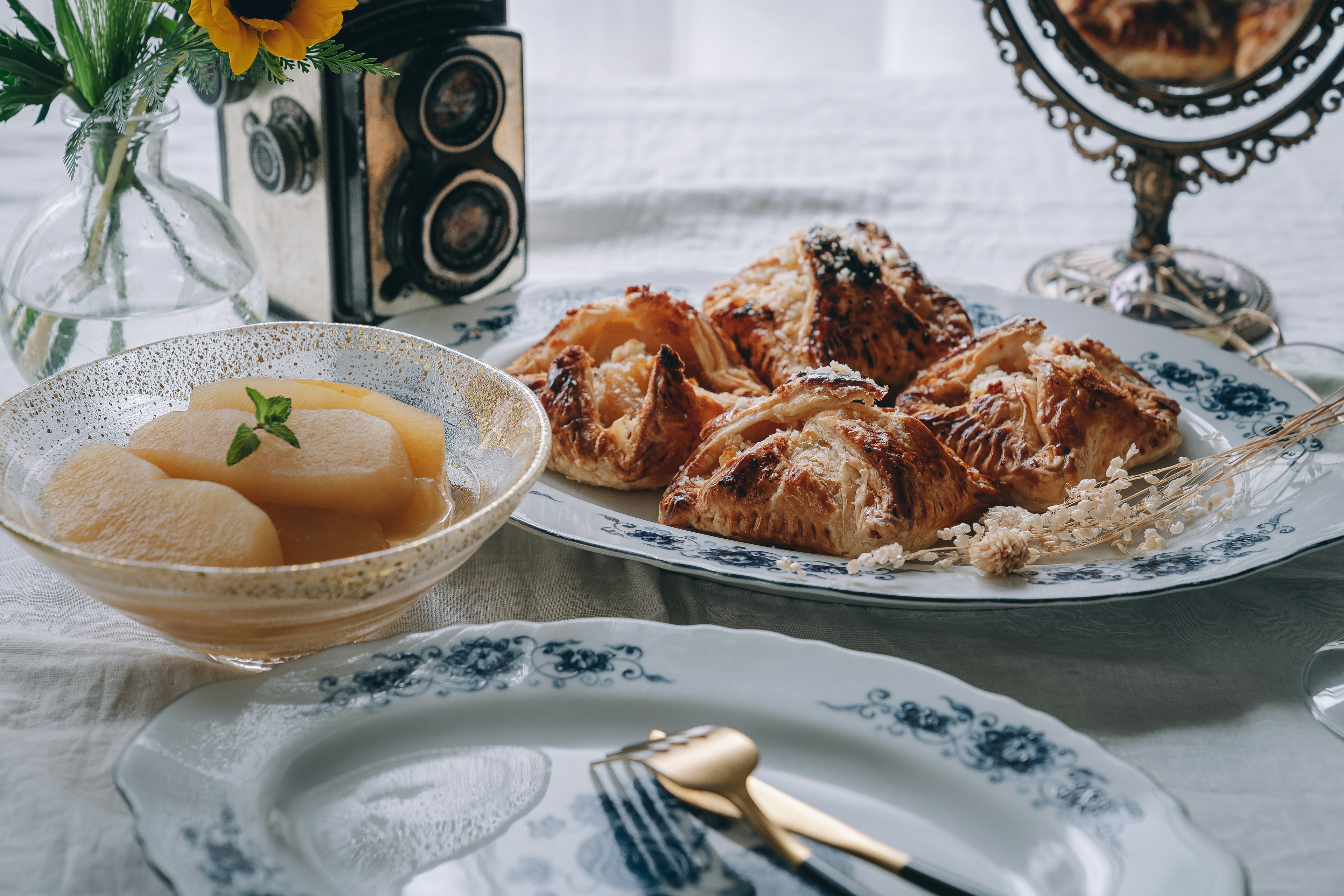 A vintage camera and vase on a table featuring beautiful pastries and fruit