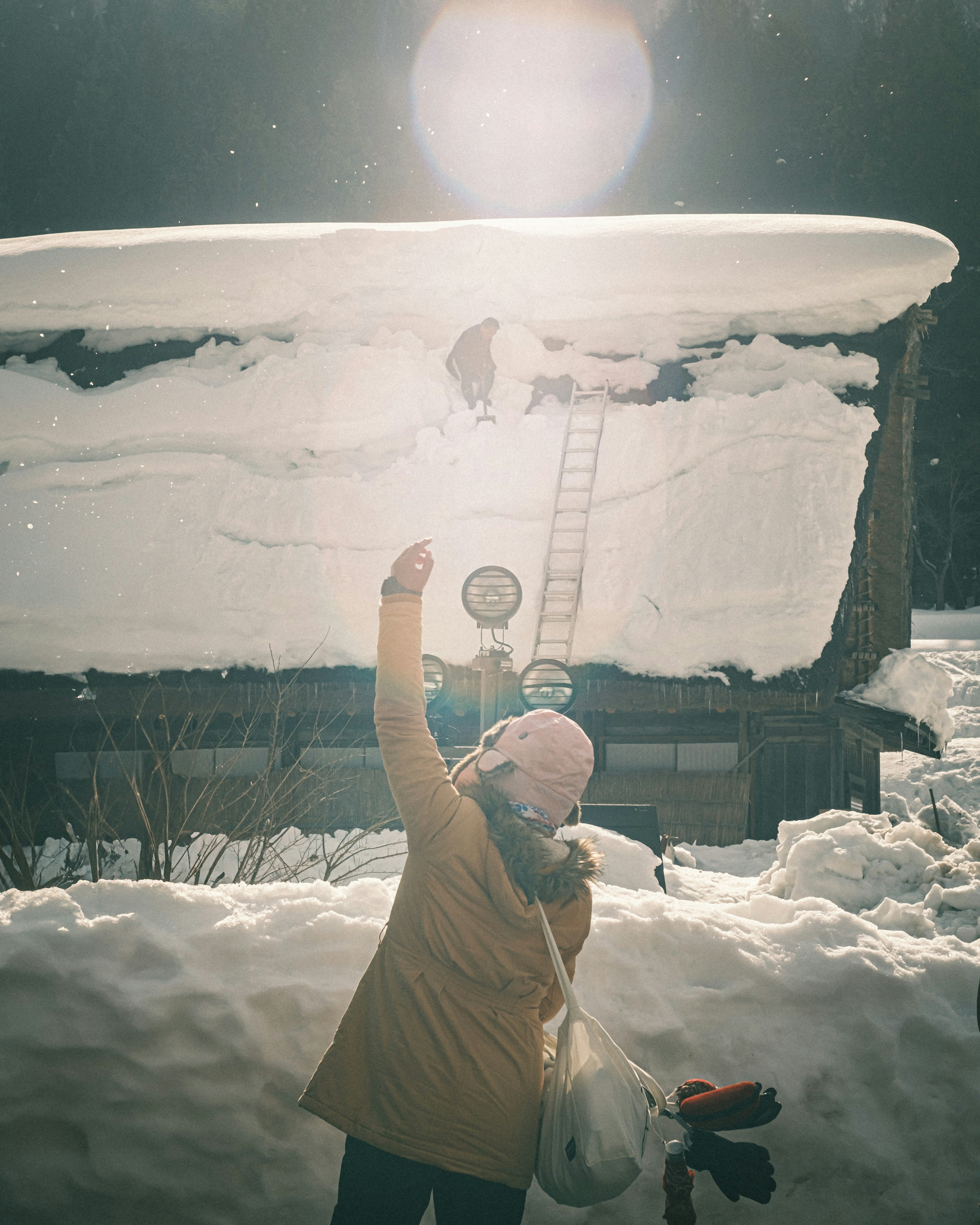 Woman looking up at a snow-covered house roof with a ladder in winter