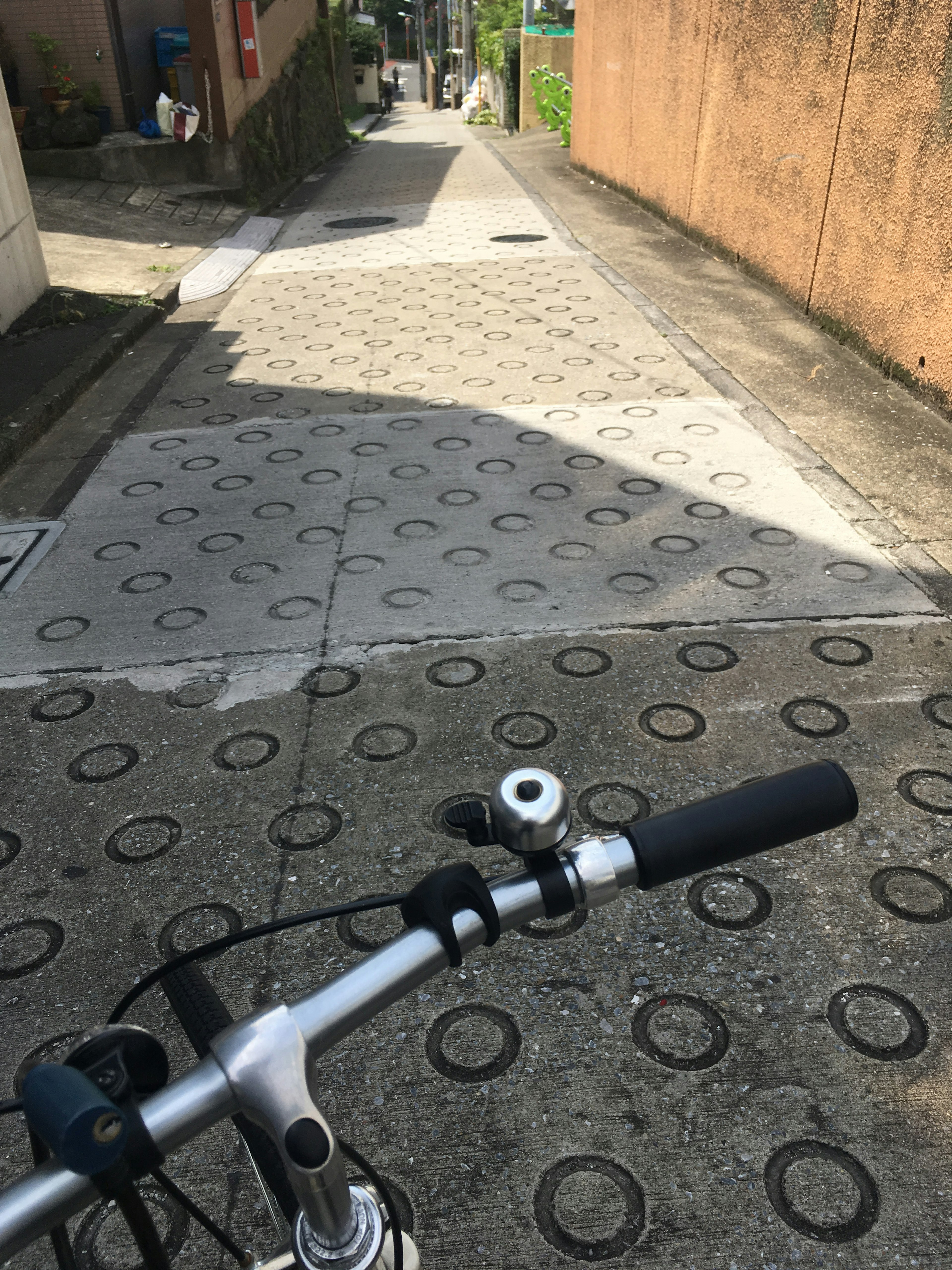 View from a bicycle handlebar showing an inclined road with circular patterned pavement