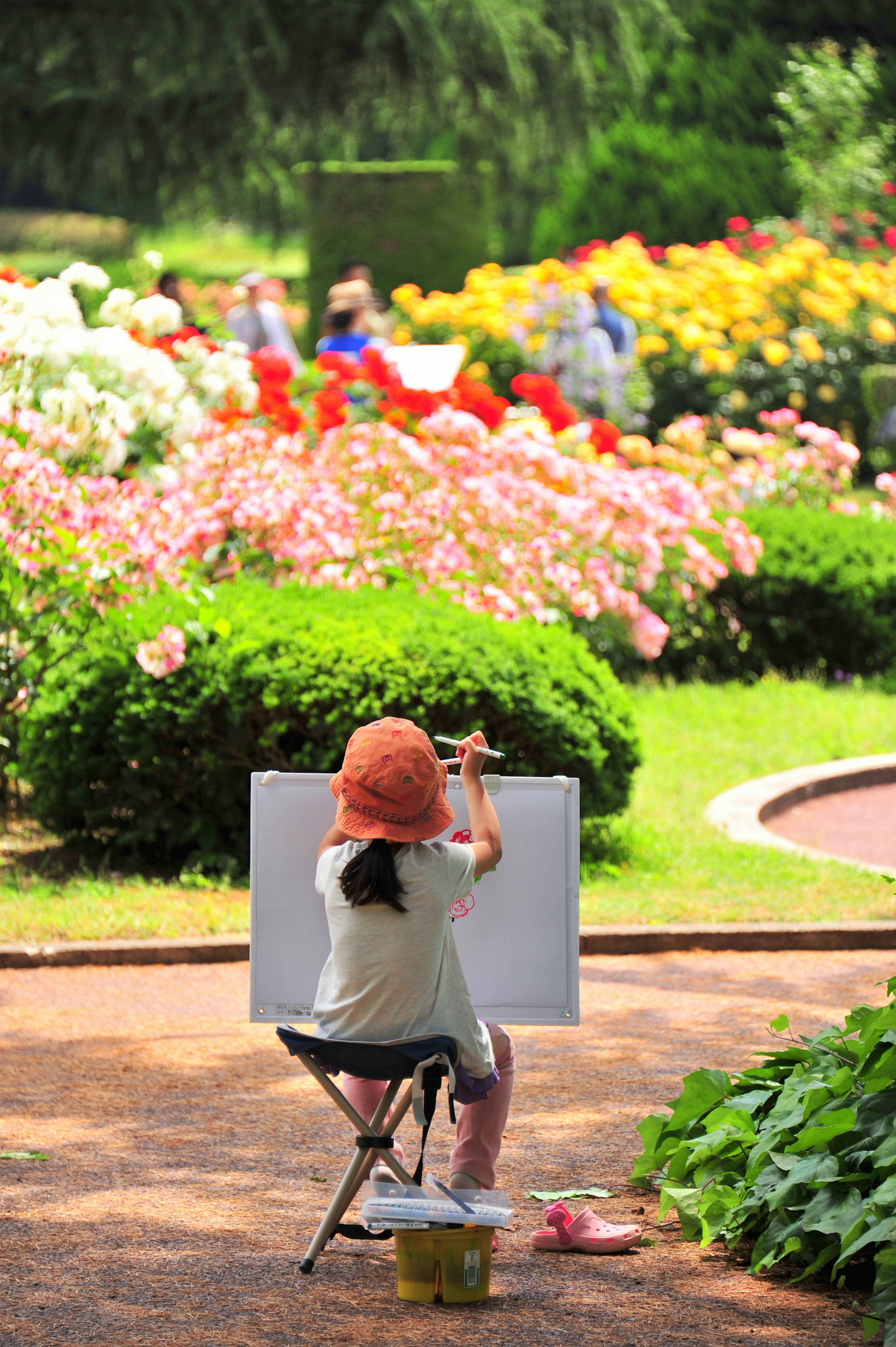 Child painting in a park surrounded by colorful flowers