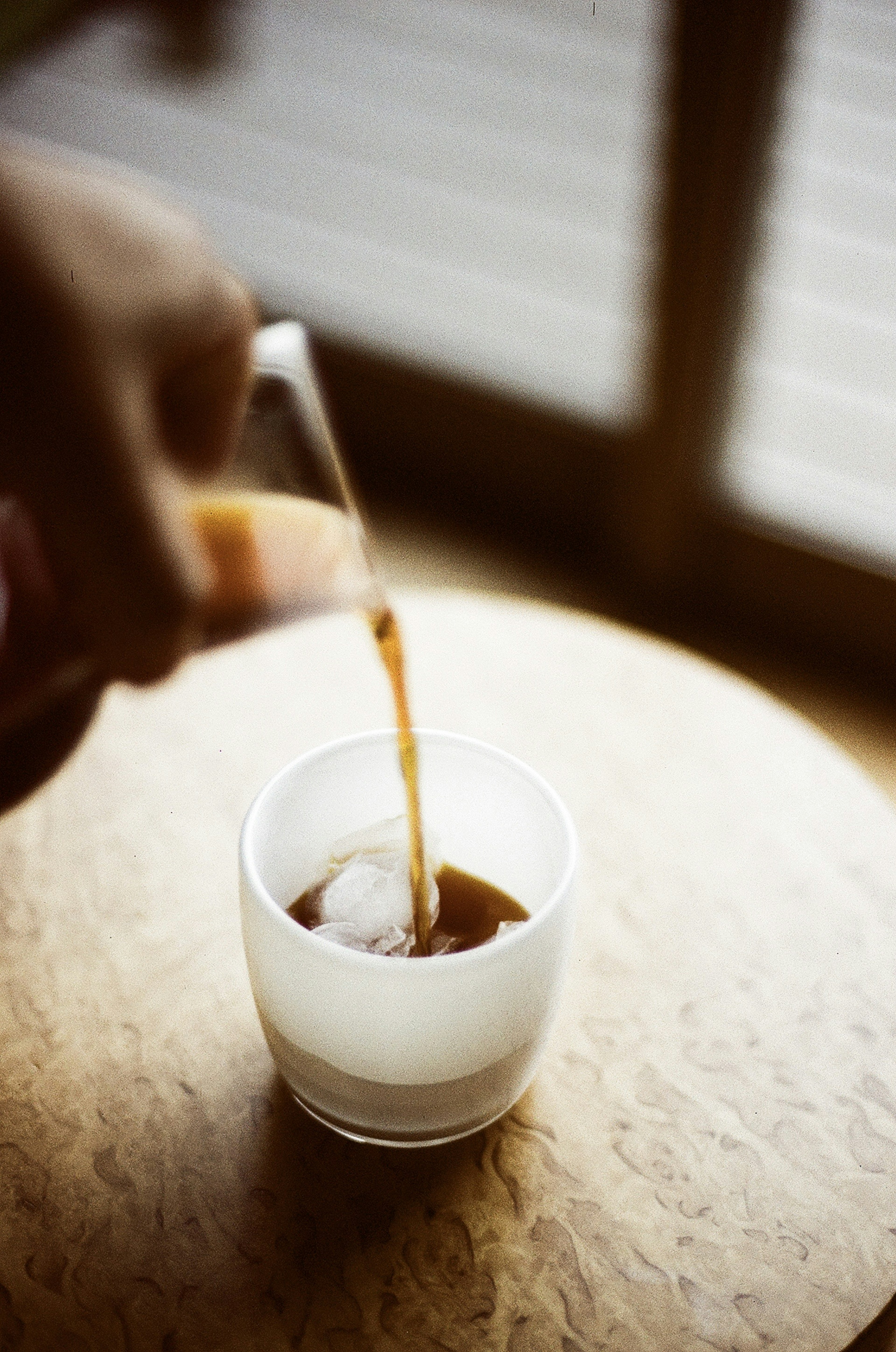 Hand pouring coffee into a glass with ice