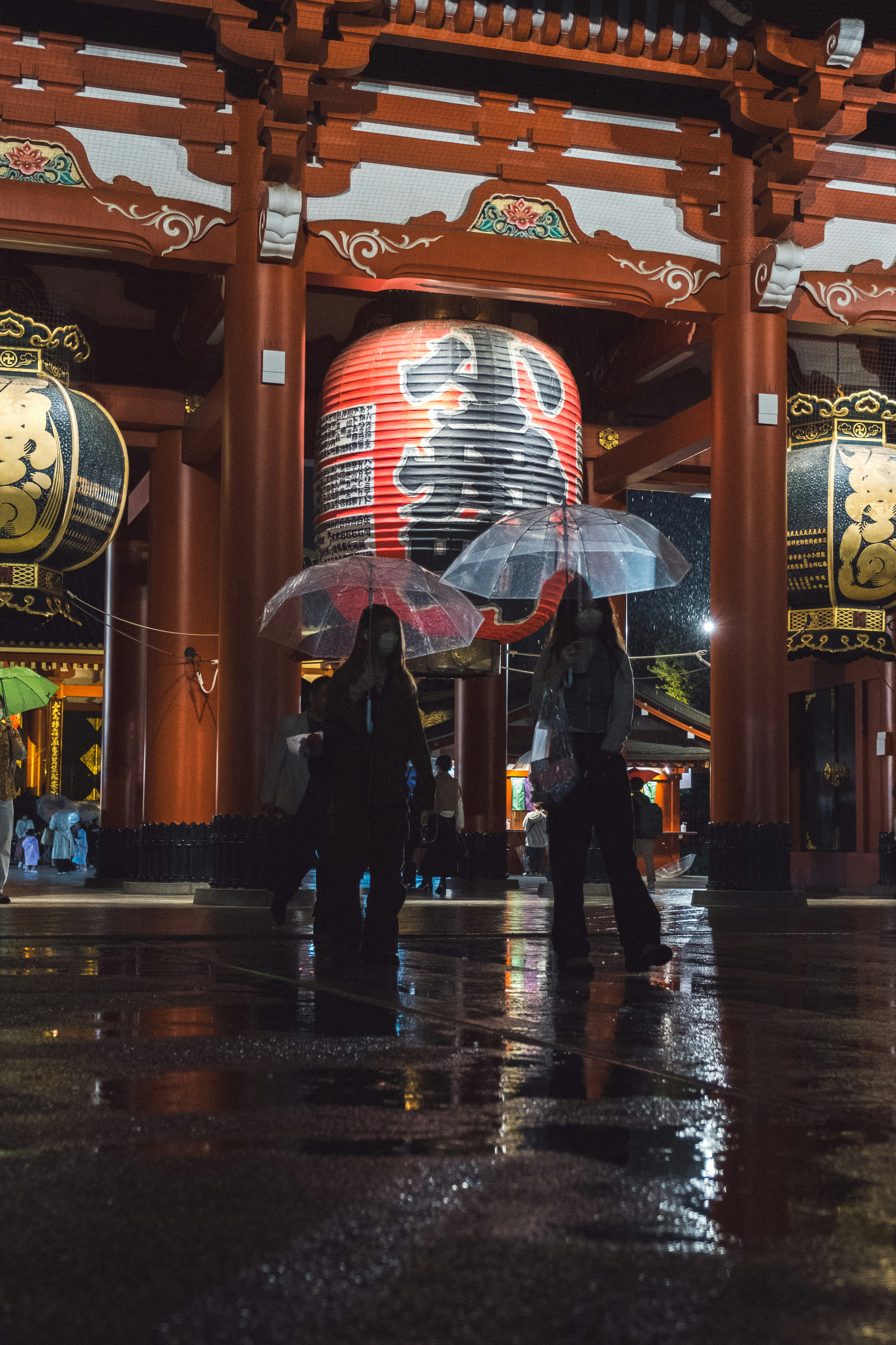 Dua orang memegang payung di depan Kuil Senso-ji di malam hari