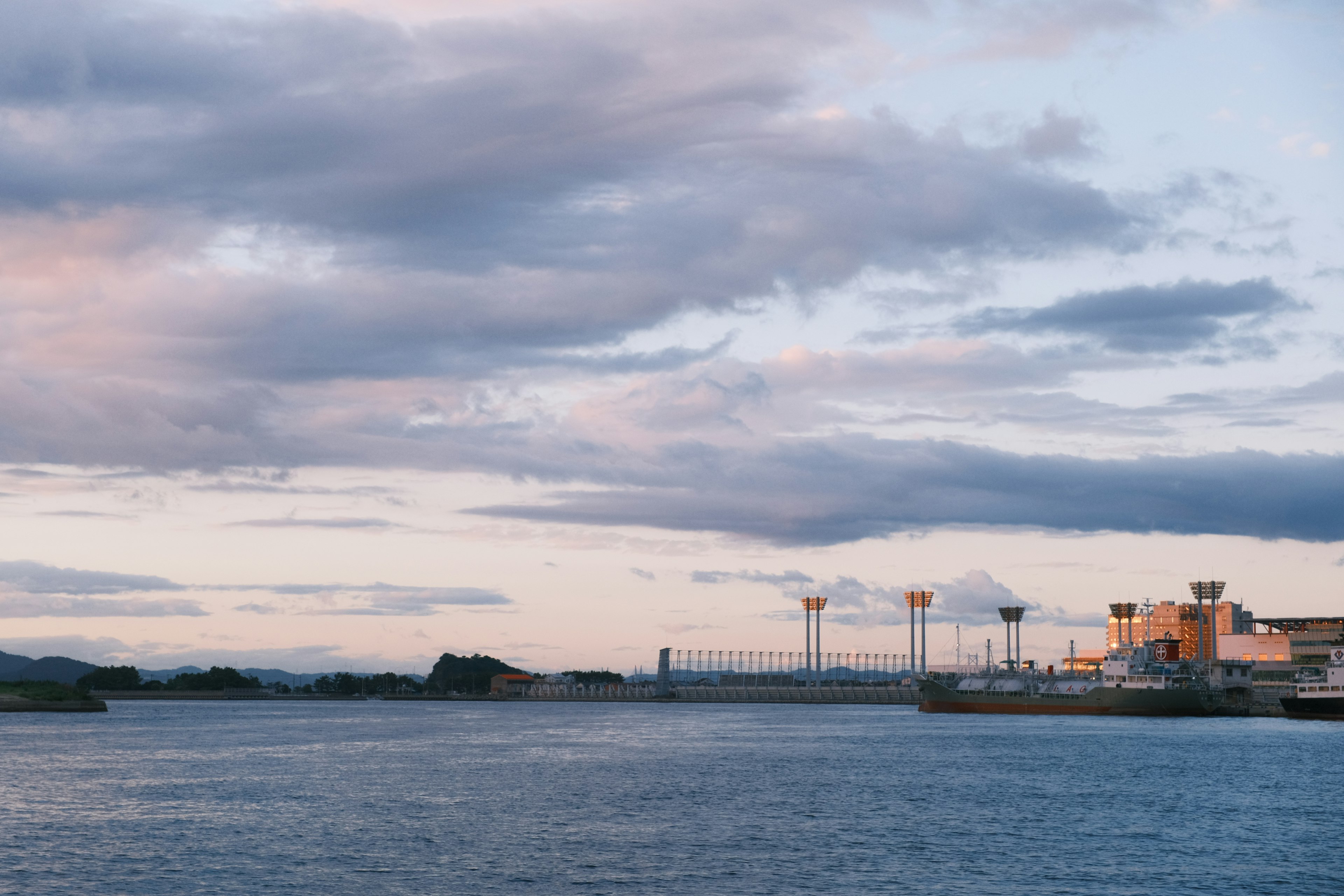 Vista escénica de un río con edificios industriales bajo un cielo colorido al atardecer