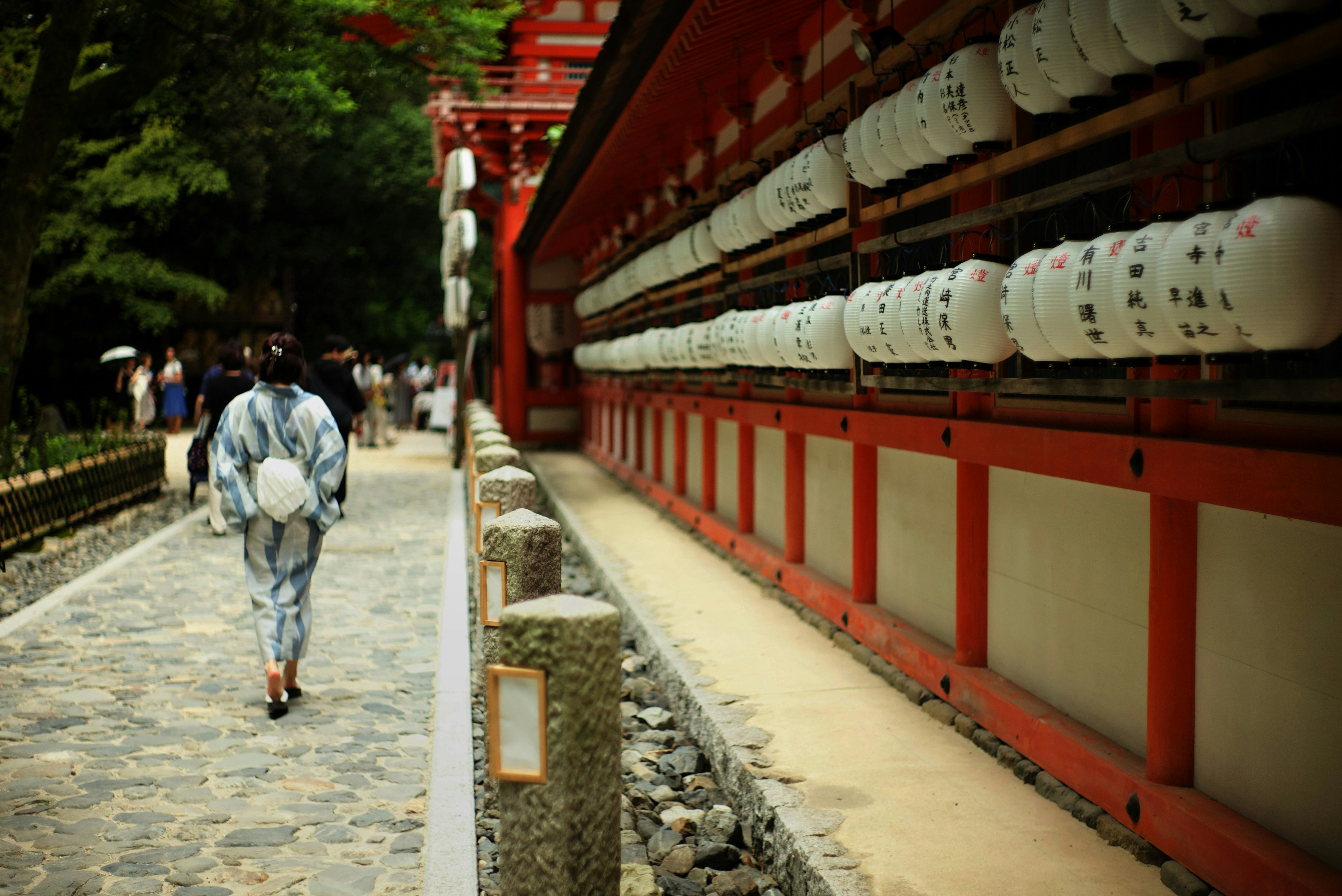 Una persona con yukata tradicional caminando por un sendero del santuario con edificios rojos