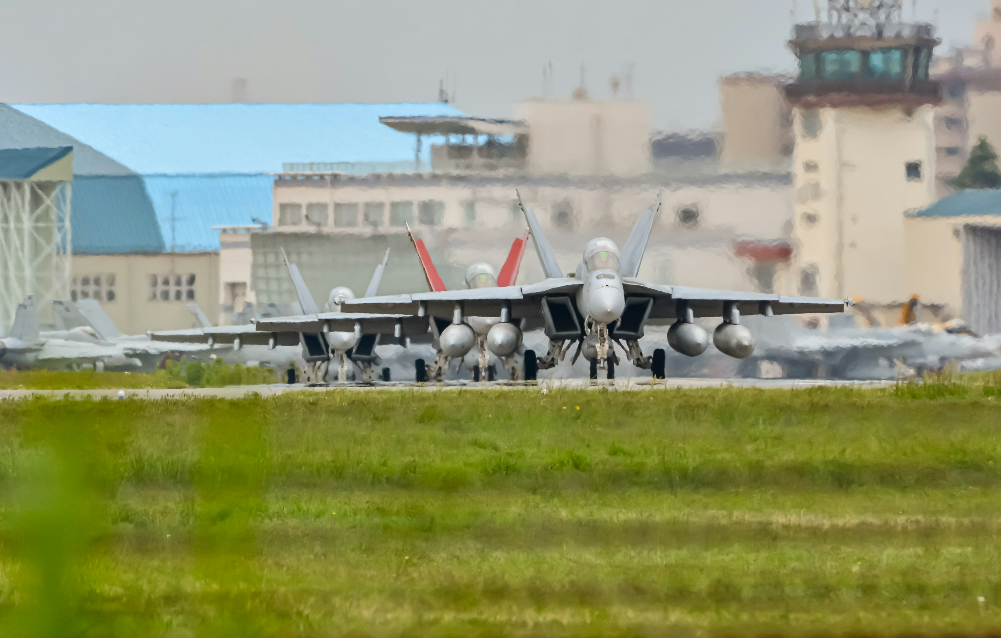 Military airfield with fighter jets lined up and buildings in the background