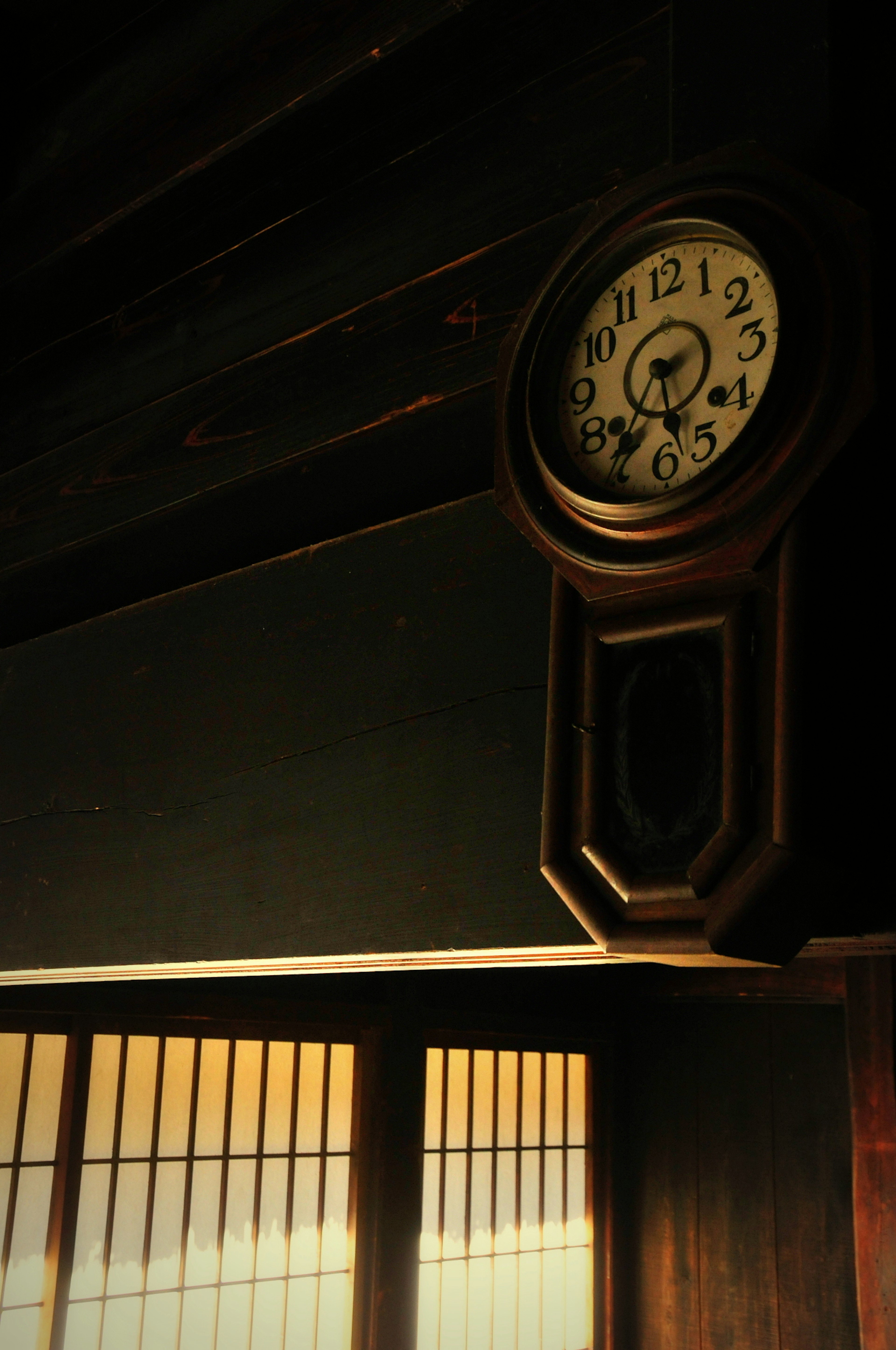 A wooden wall clock hanging in a dimly lit room