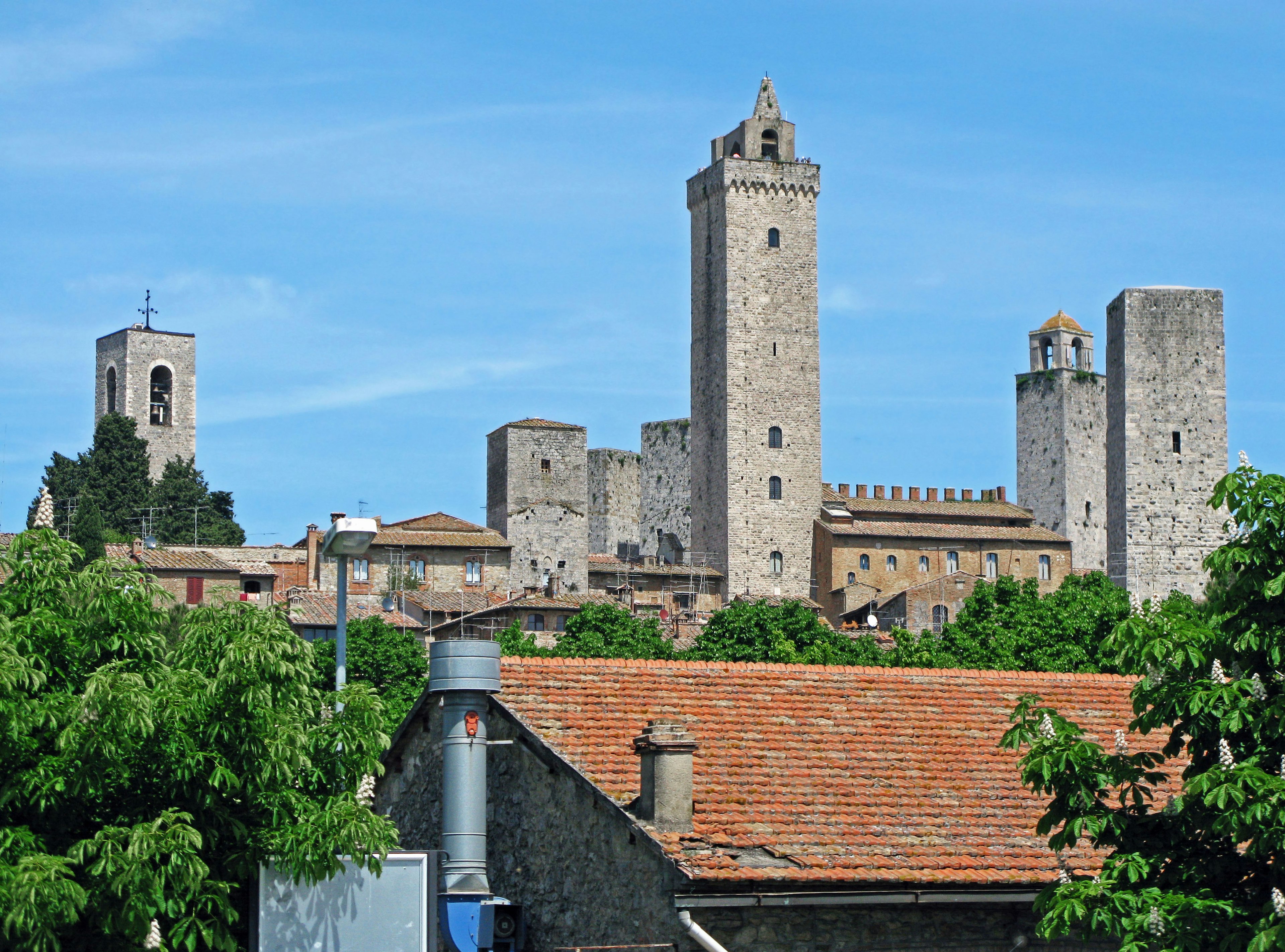 Tours médiévales et murs de San Gimignano en Toscane entourés d'arbres verts et d'un ciel bleu