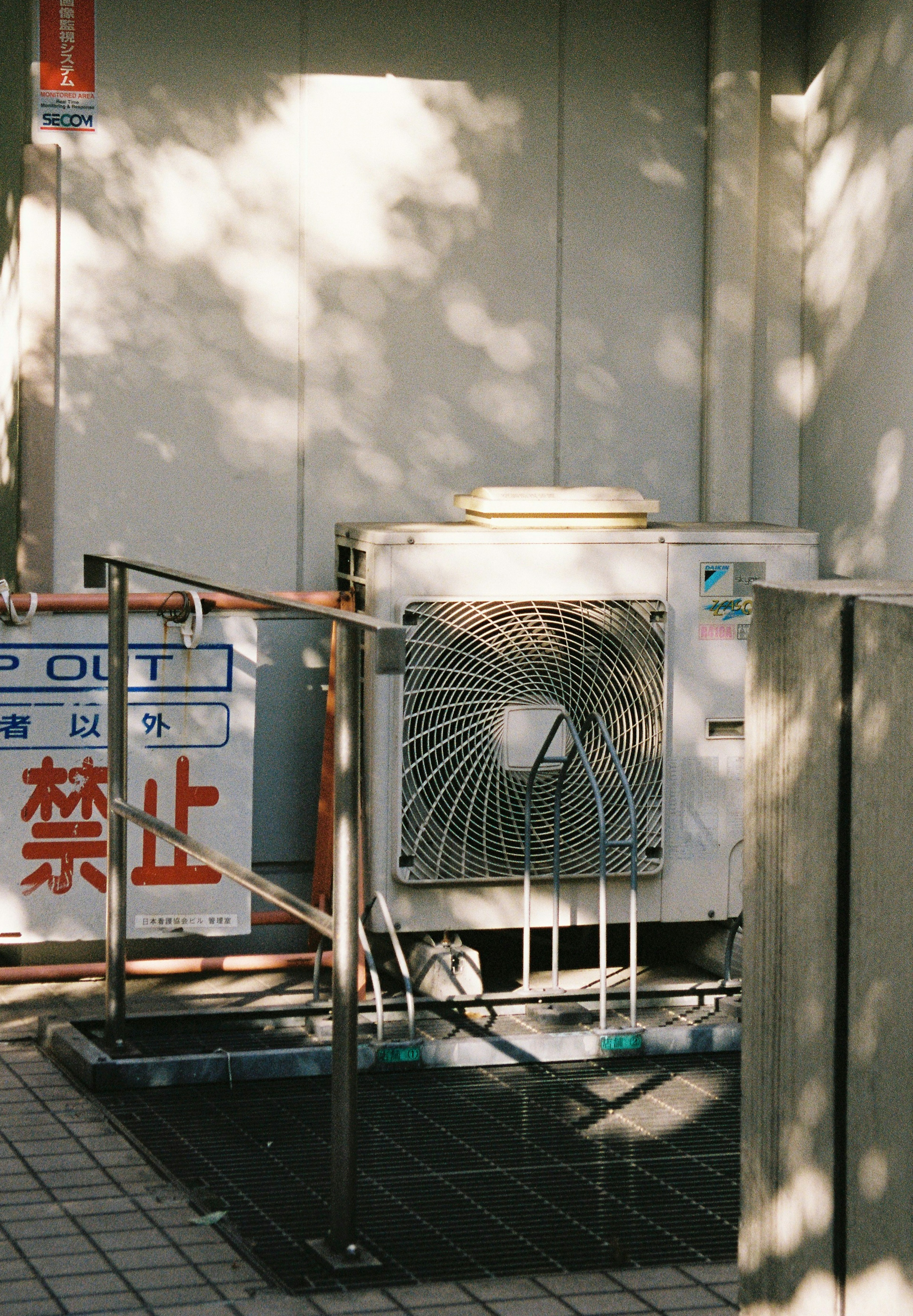 Air conditioning unit against a concrete wall with a metal railing