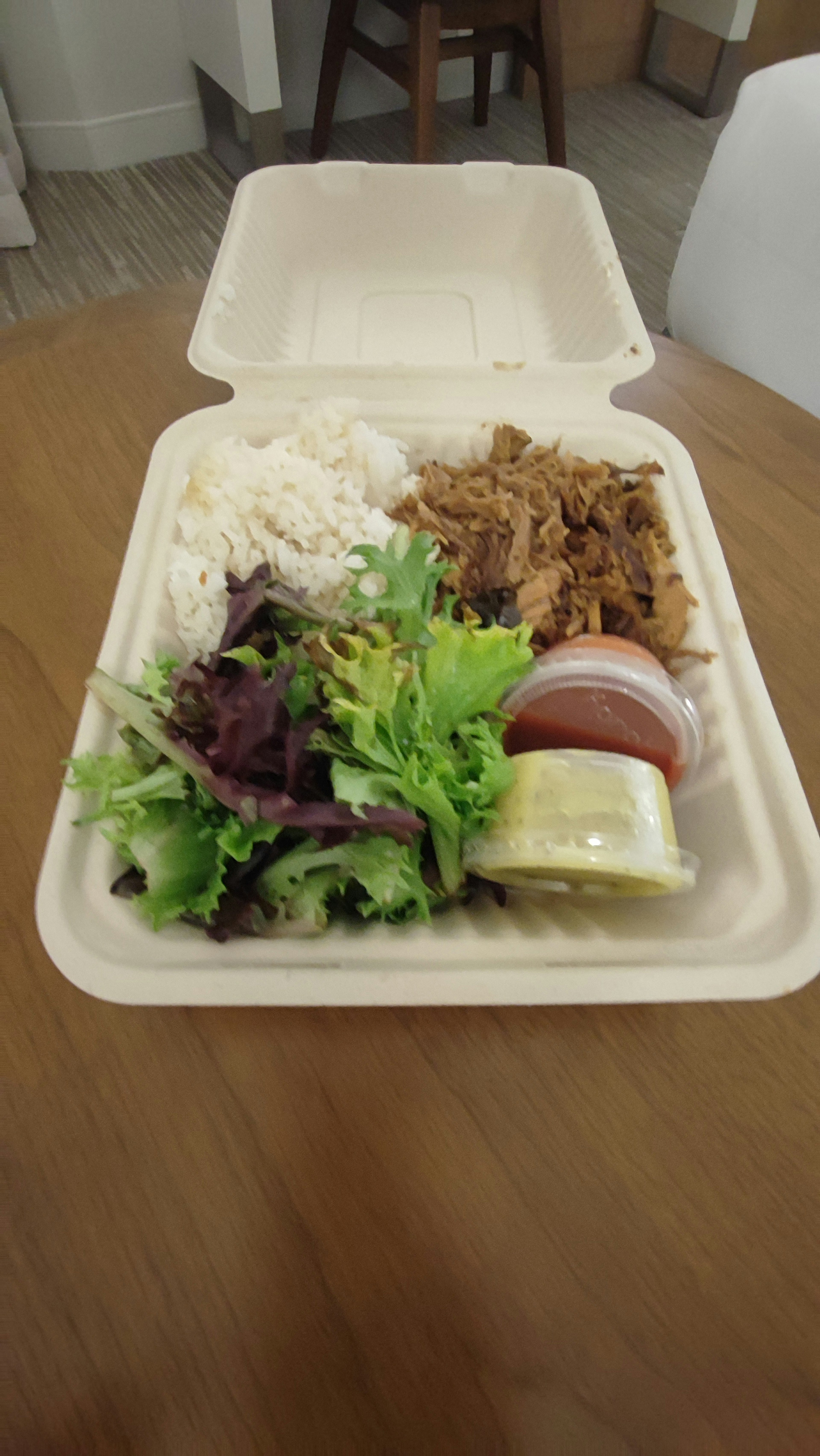 Takeout container with white rice, chicken, salad, and sauce