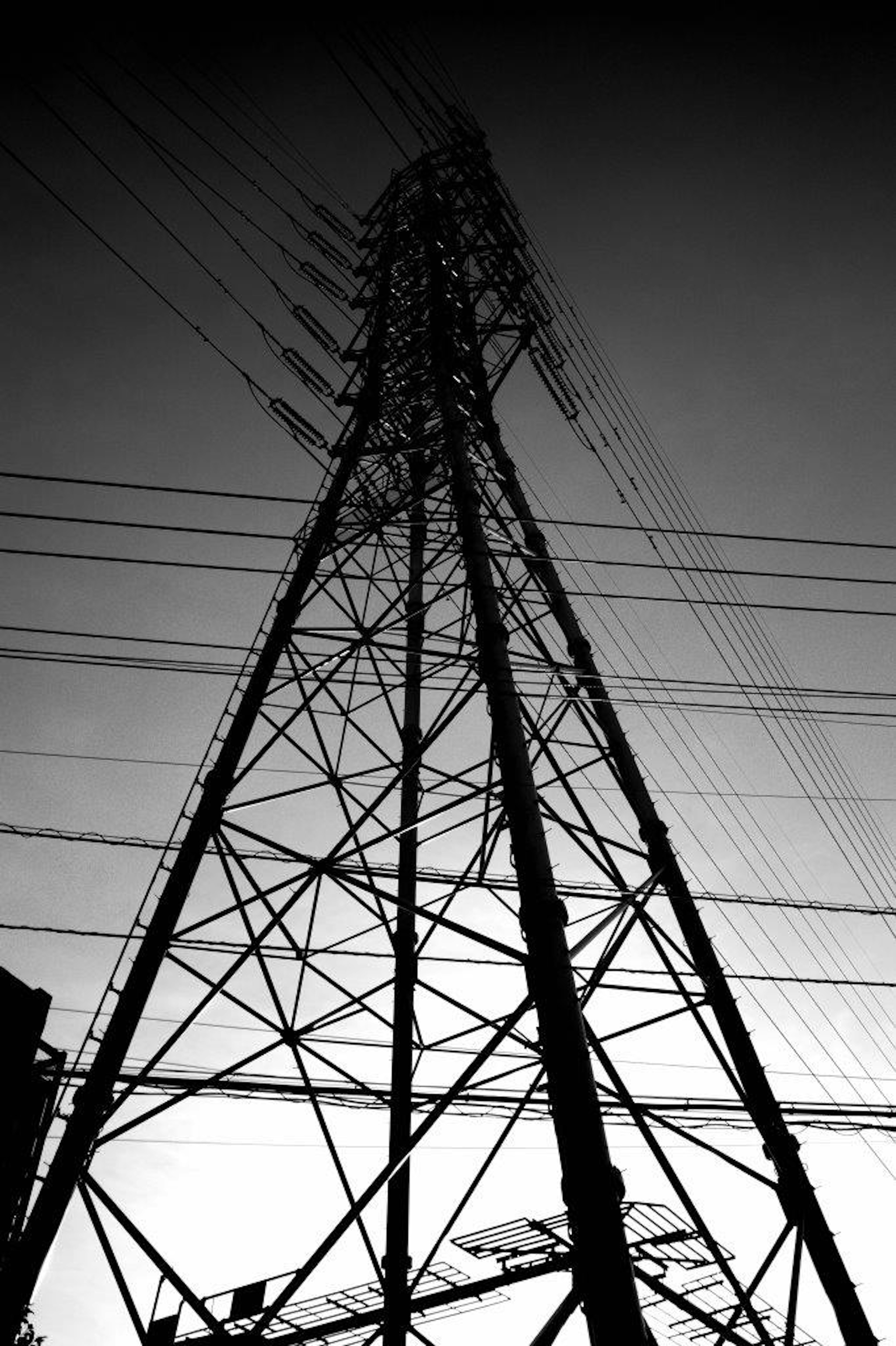 Silhouette of a high-voltage power tower against a gradient sky in black and white