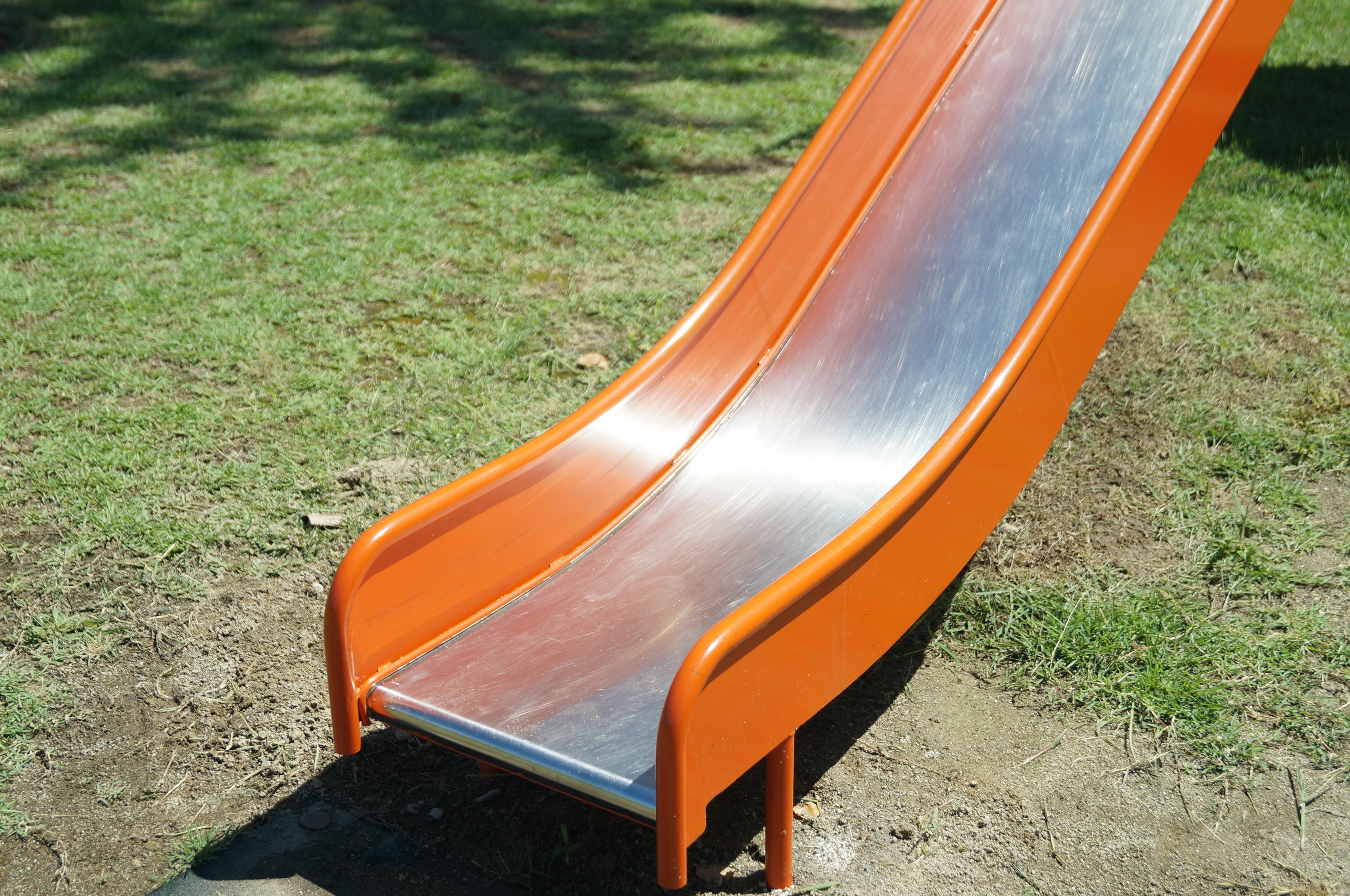 Orange slide with metal surface set on green grass