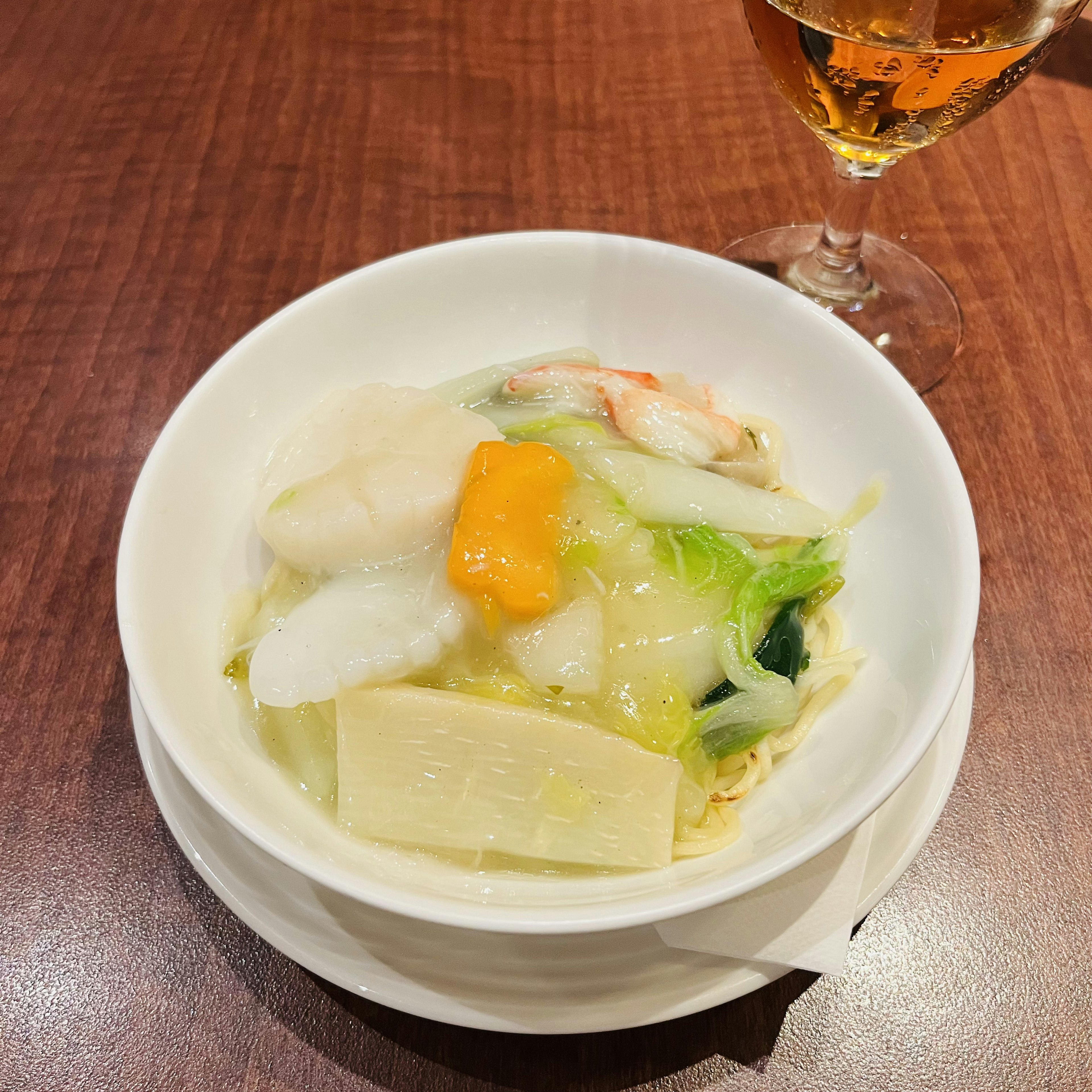 A white bowl filled with seafood and vegetable soup topped with egg yolk