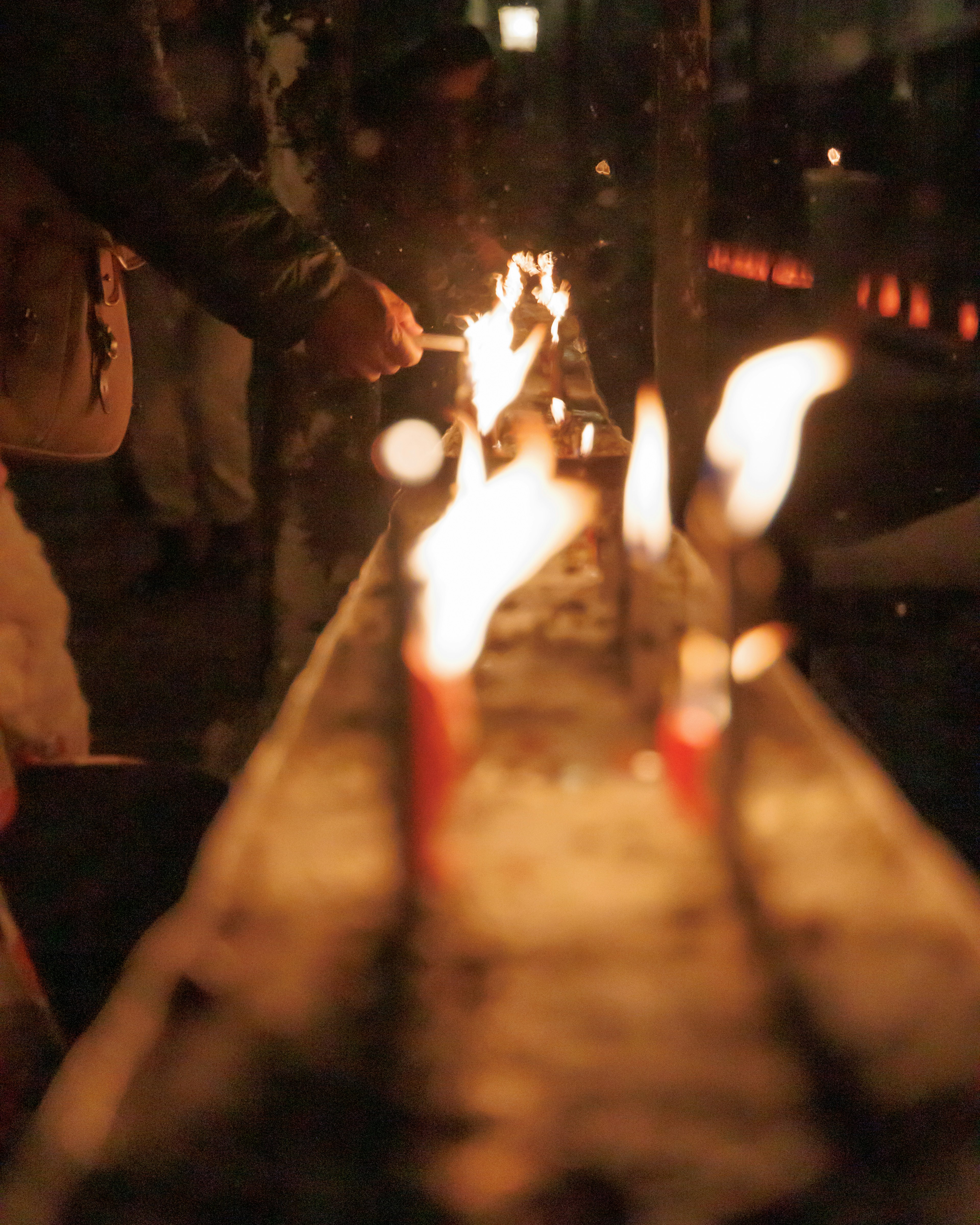 Close-up of hands lighting candles in a dimly lit setting