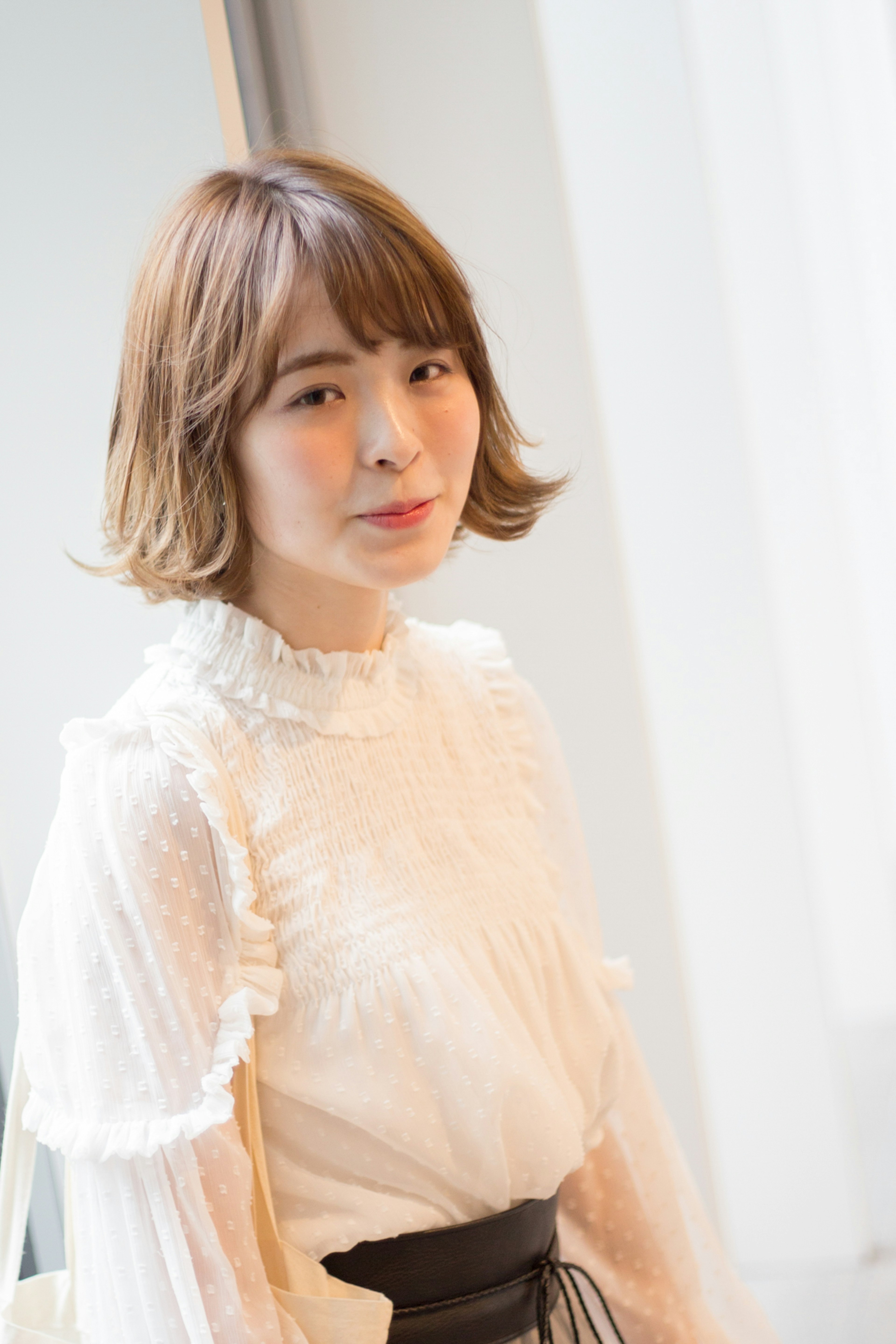 A woman smiling indoors wearing a white blouse