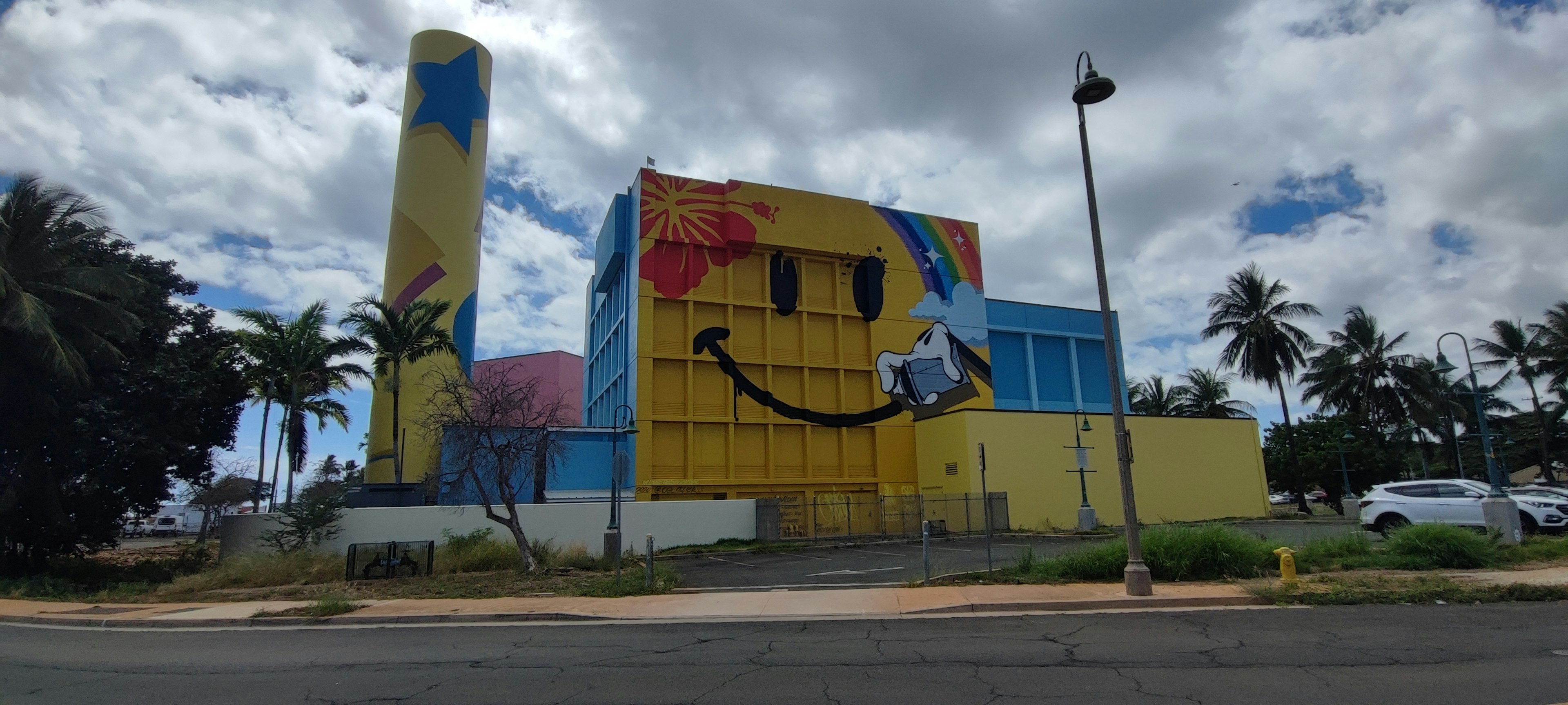 Bangunan dengan mural berwarna cerah menampilkan wajah tersenyum dan langit biru