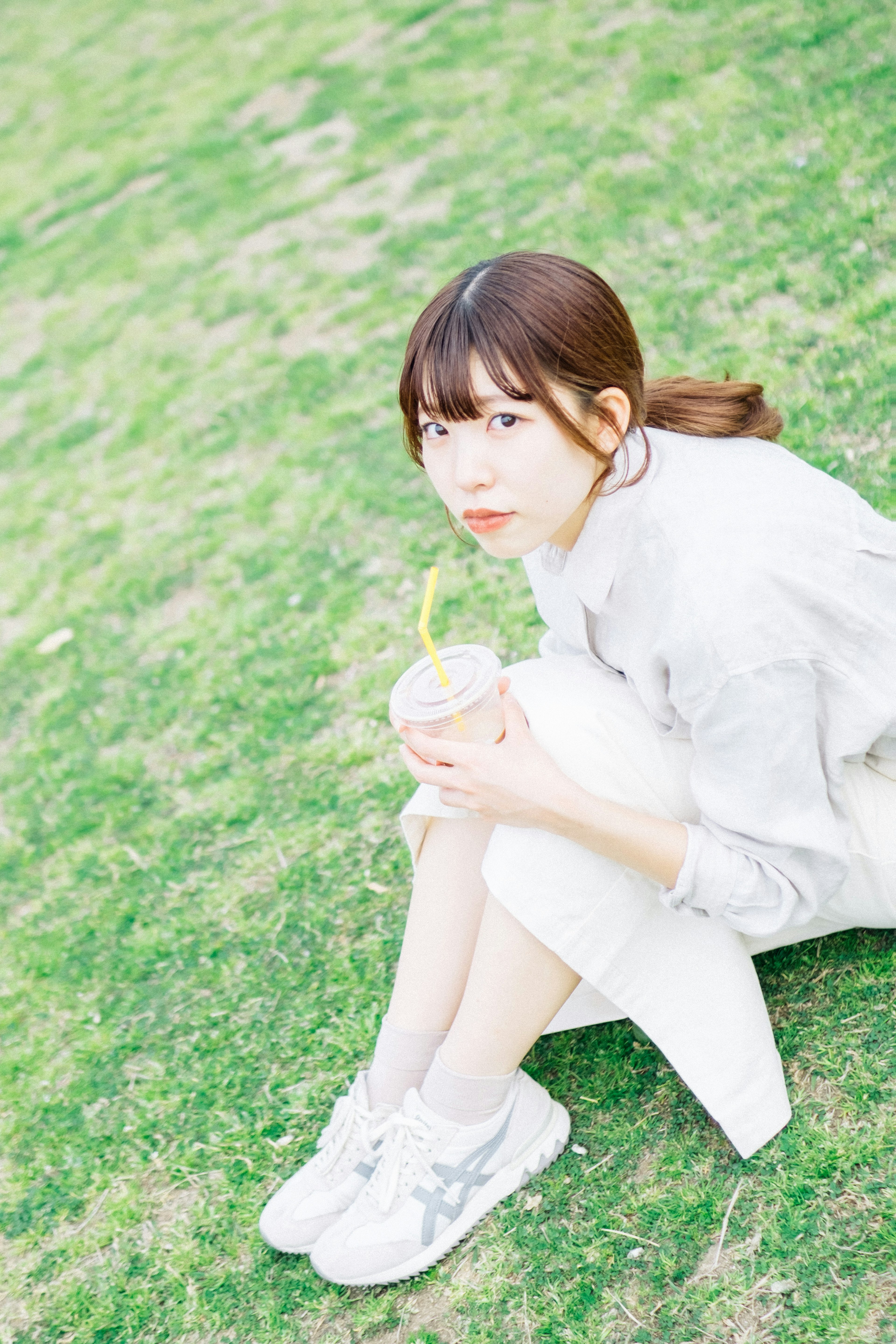 Une femme assise sur l'herbe verte tenant une boisson