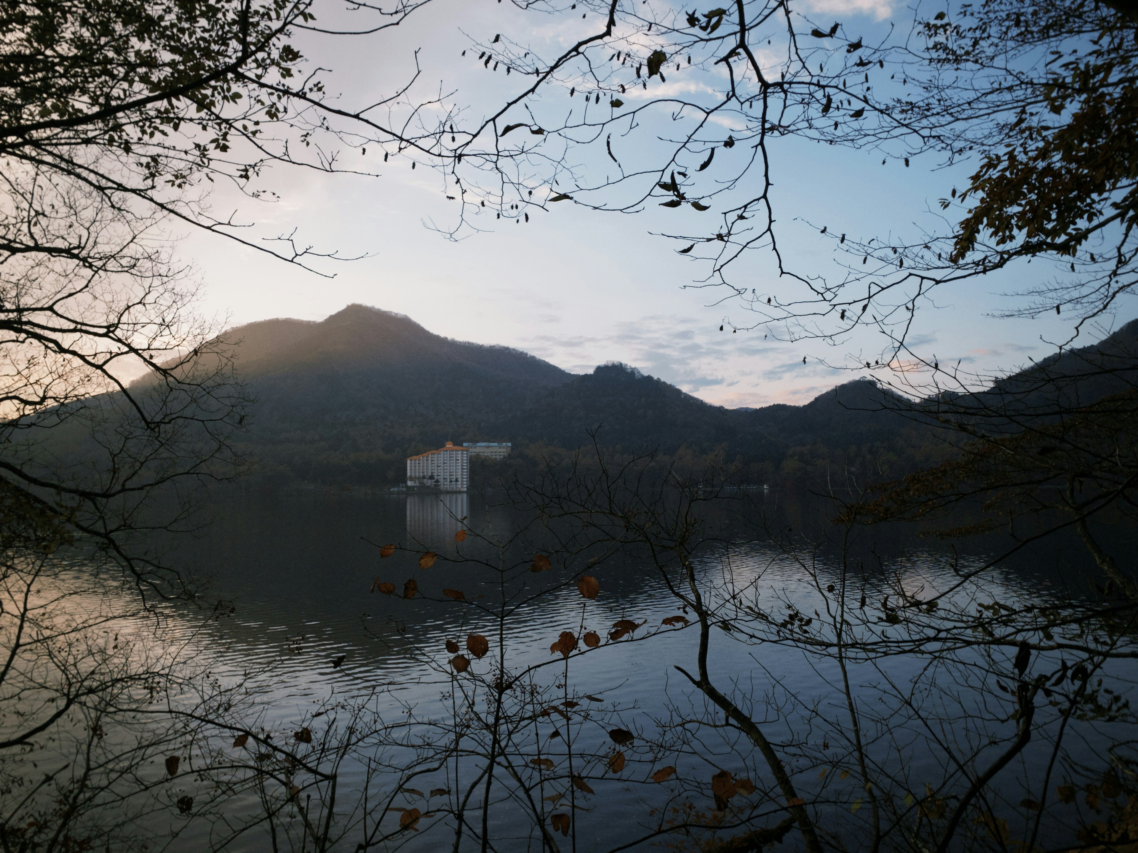 Vista serena di un lago e montagne con un edificio in controluce al crepuscolo