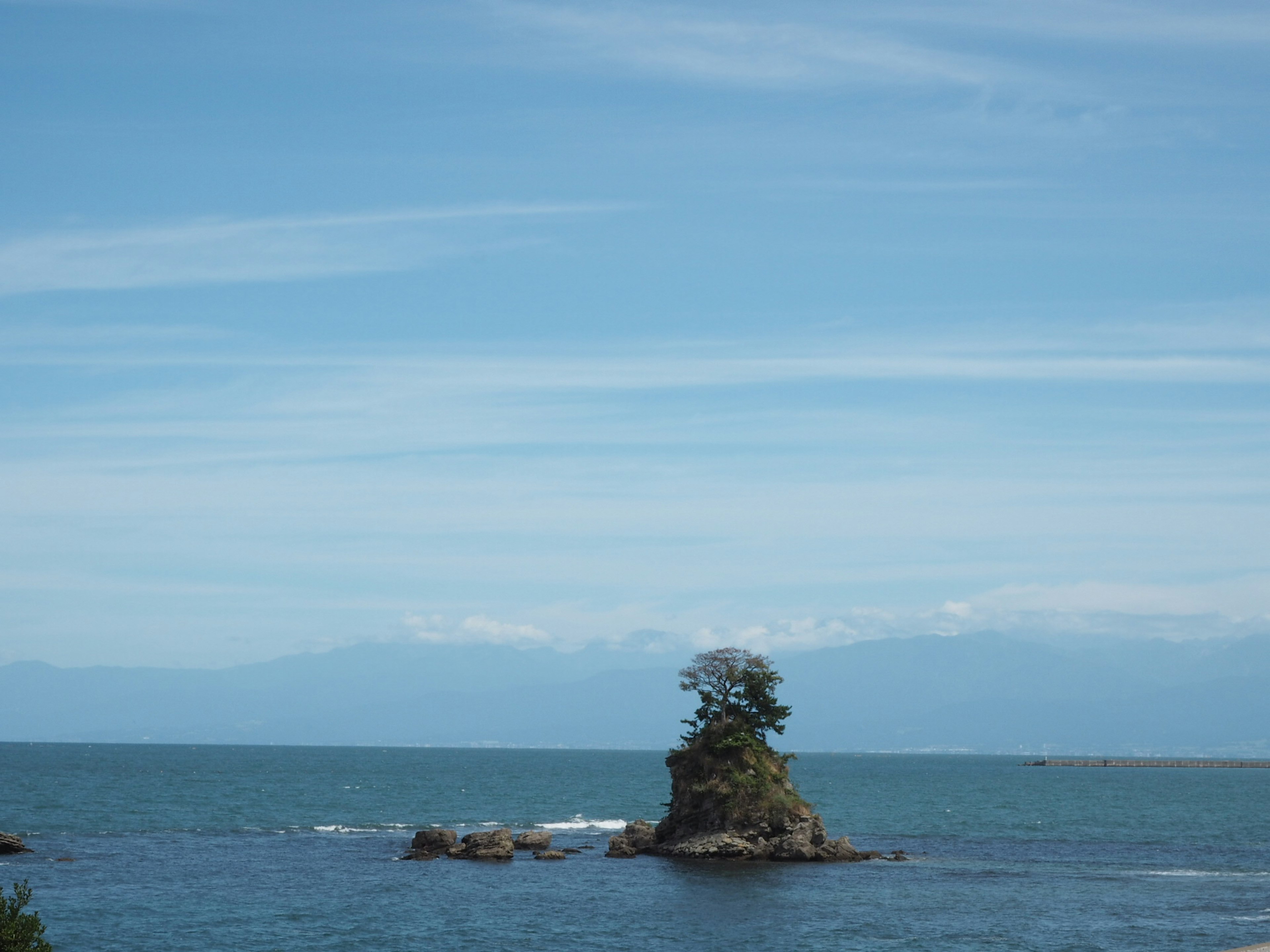 A small island with trees surrounded by blue sea and distant mountains