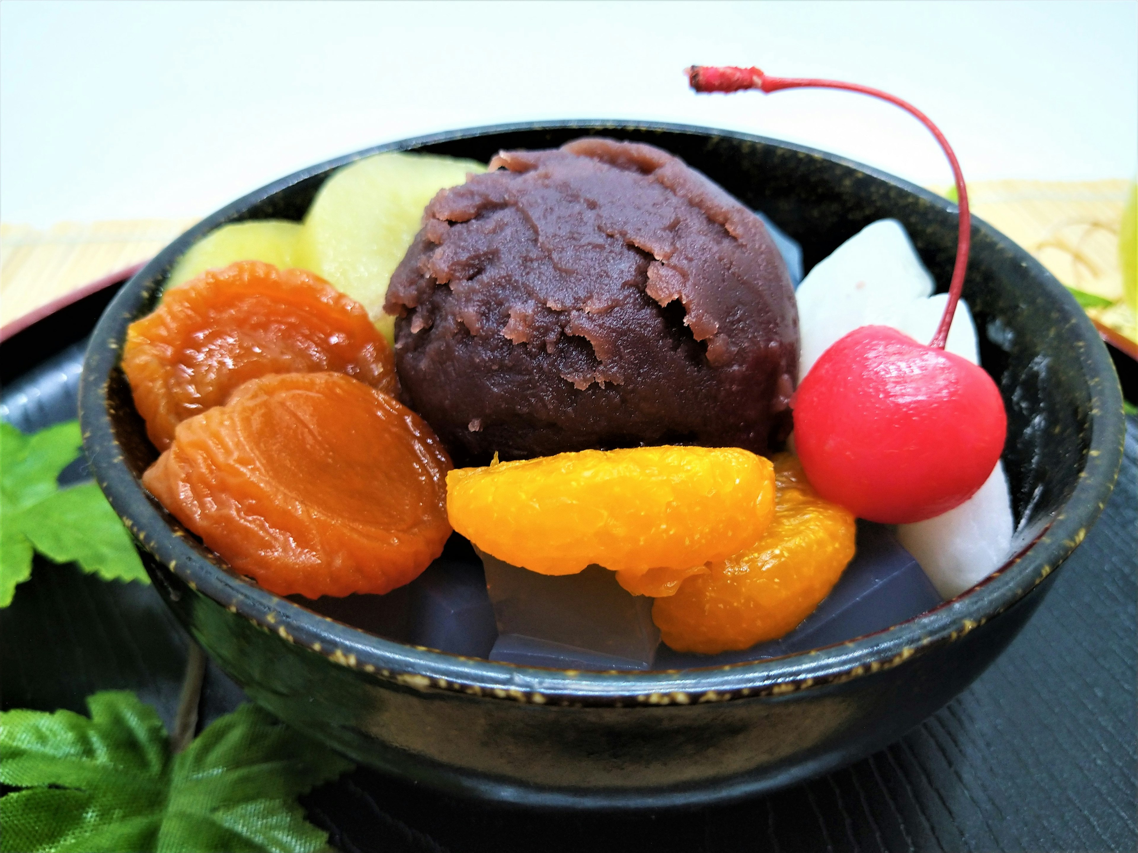 Dessert with sweet red bean paste and assorted fruits in a black bowl