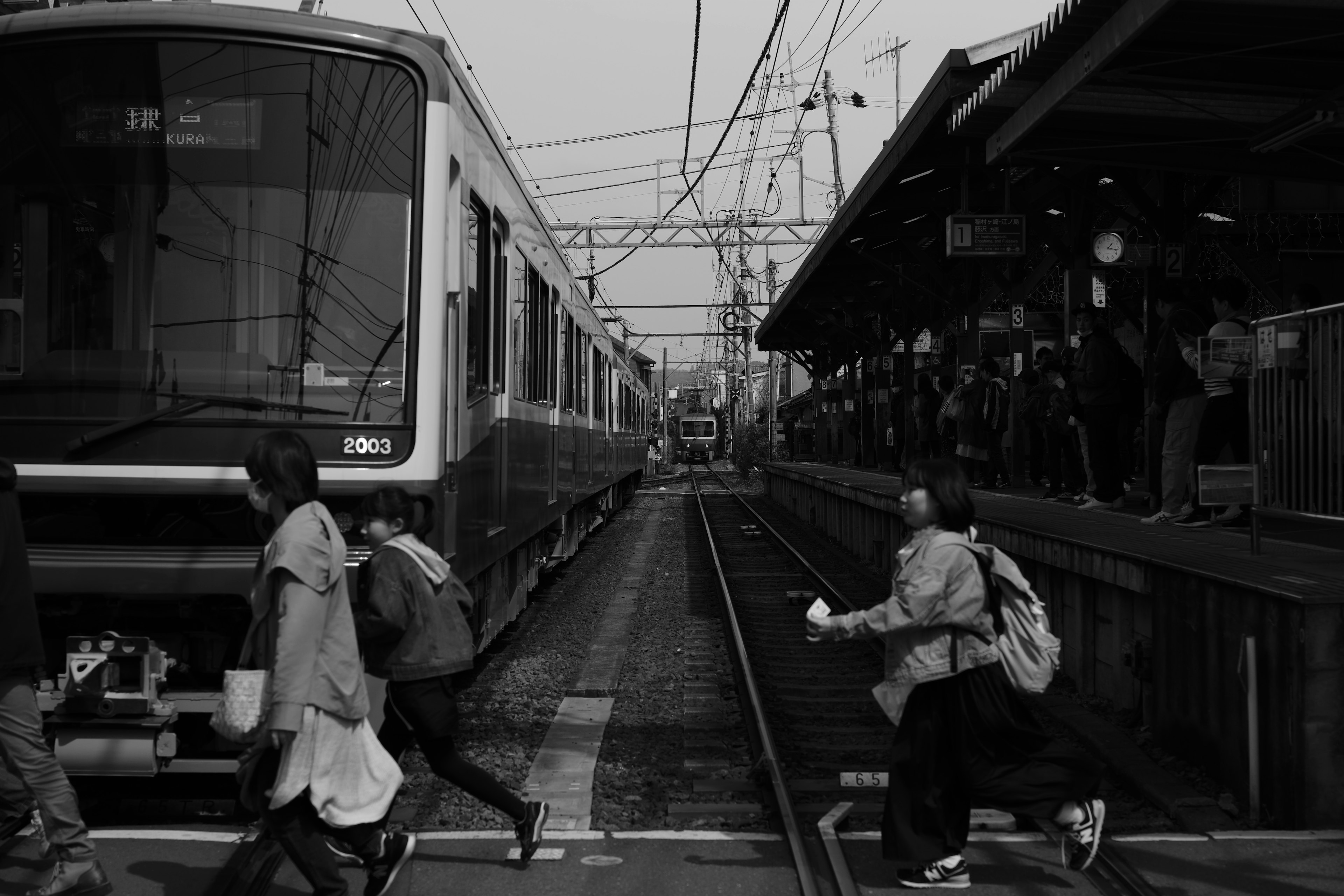 白黒の駅で電車が停車し、乗客がホームを横切っている