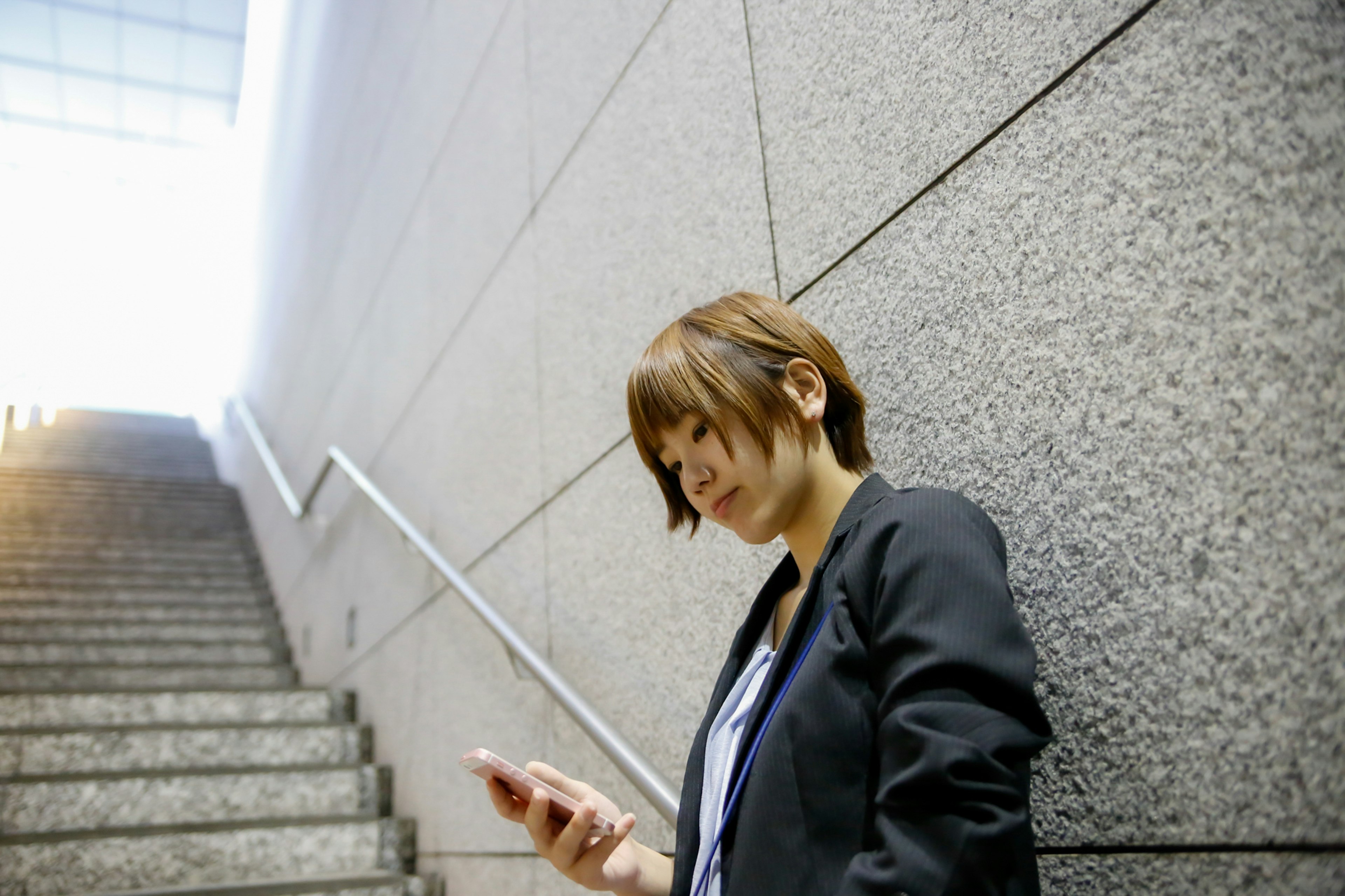 A female business person using a smartphone while standing on stairs