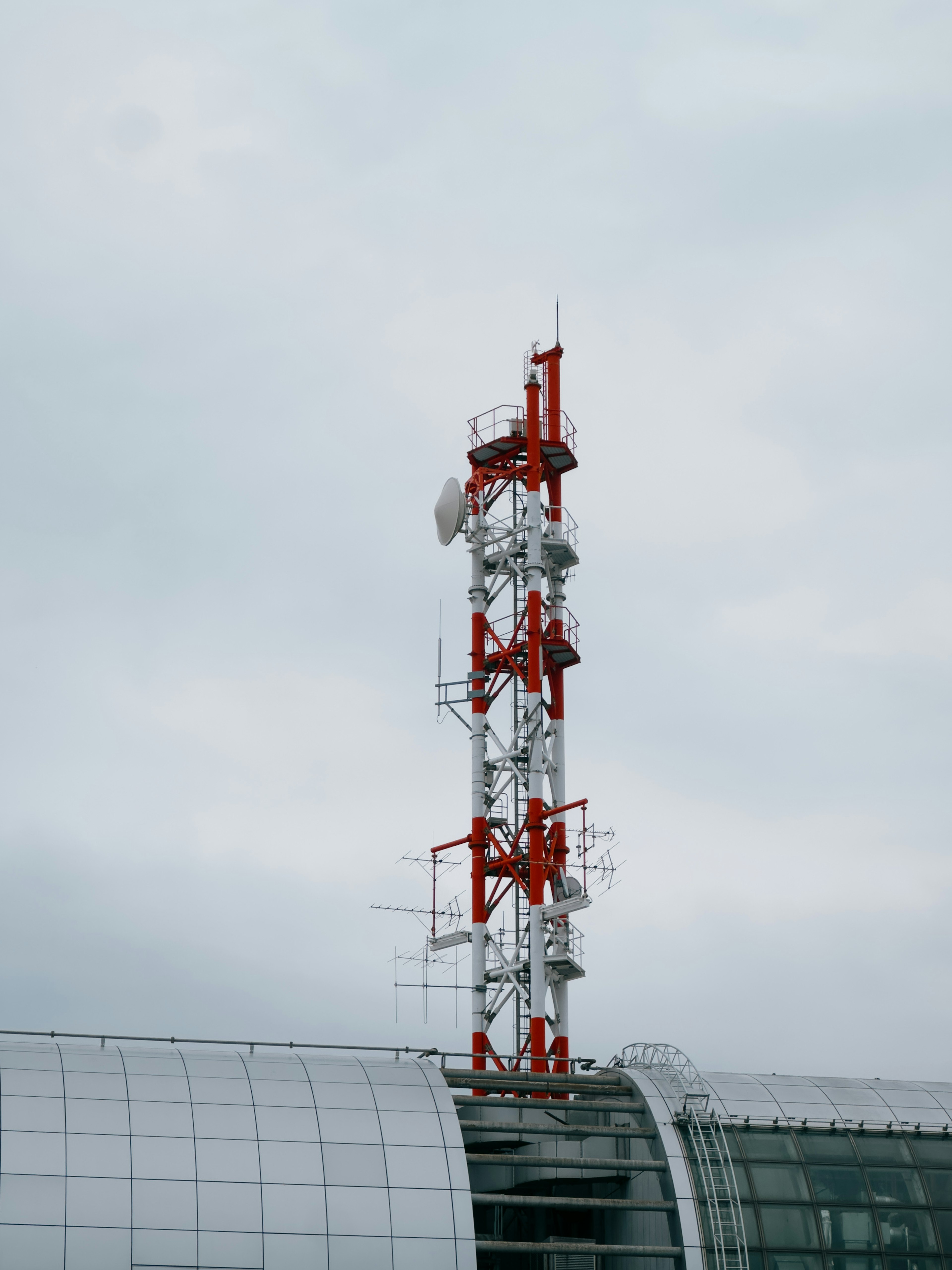 Tour de communication rouge et blanche sous un ciel nuageux