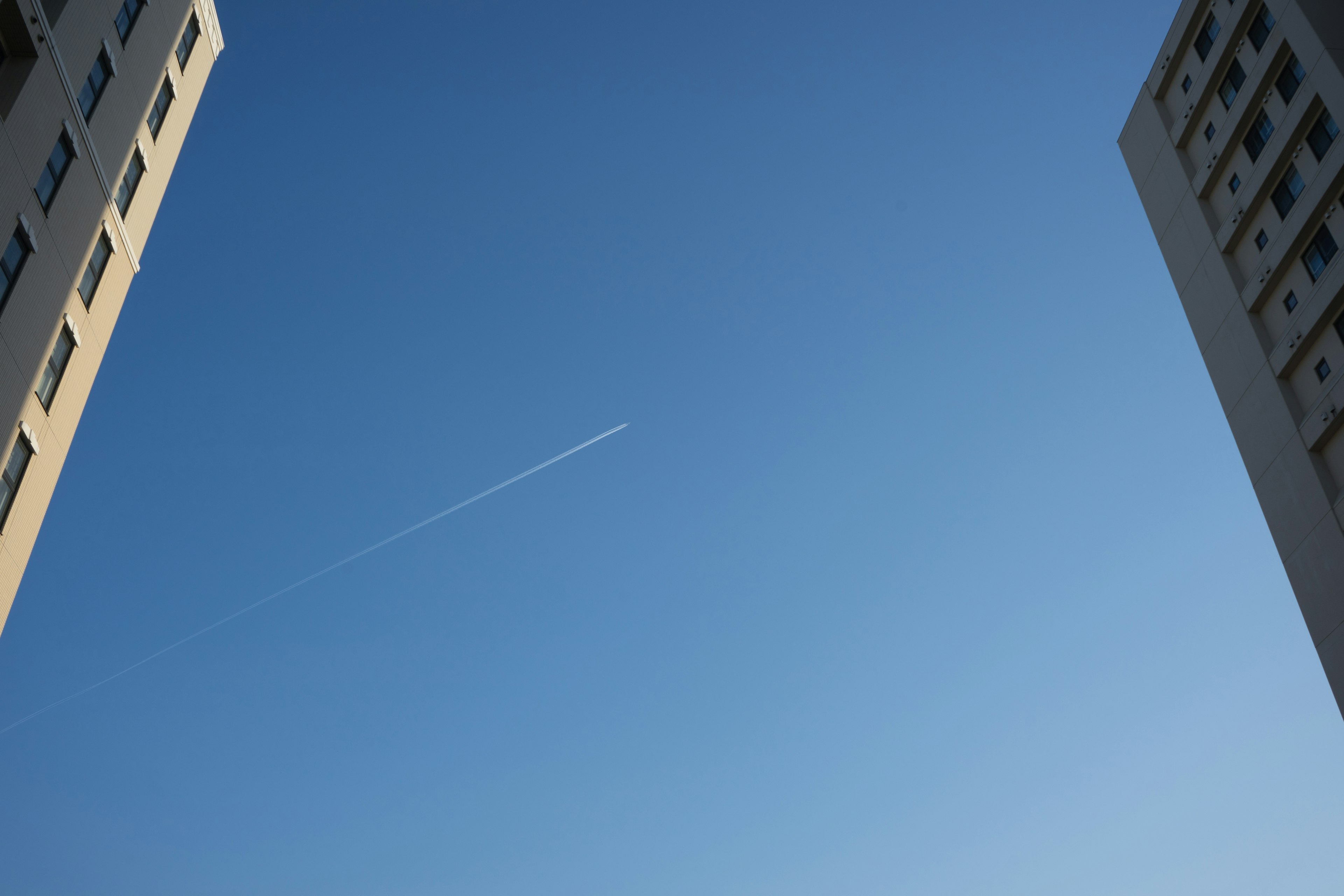 青空に飛行機雲が見えるビルの間の景色