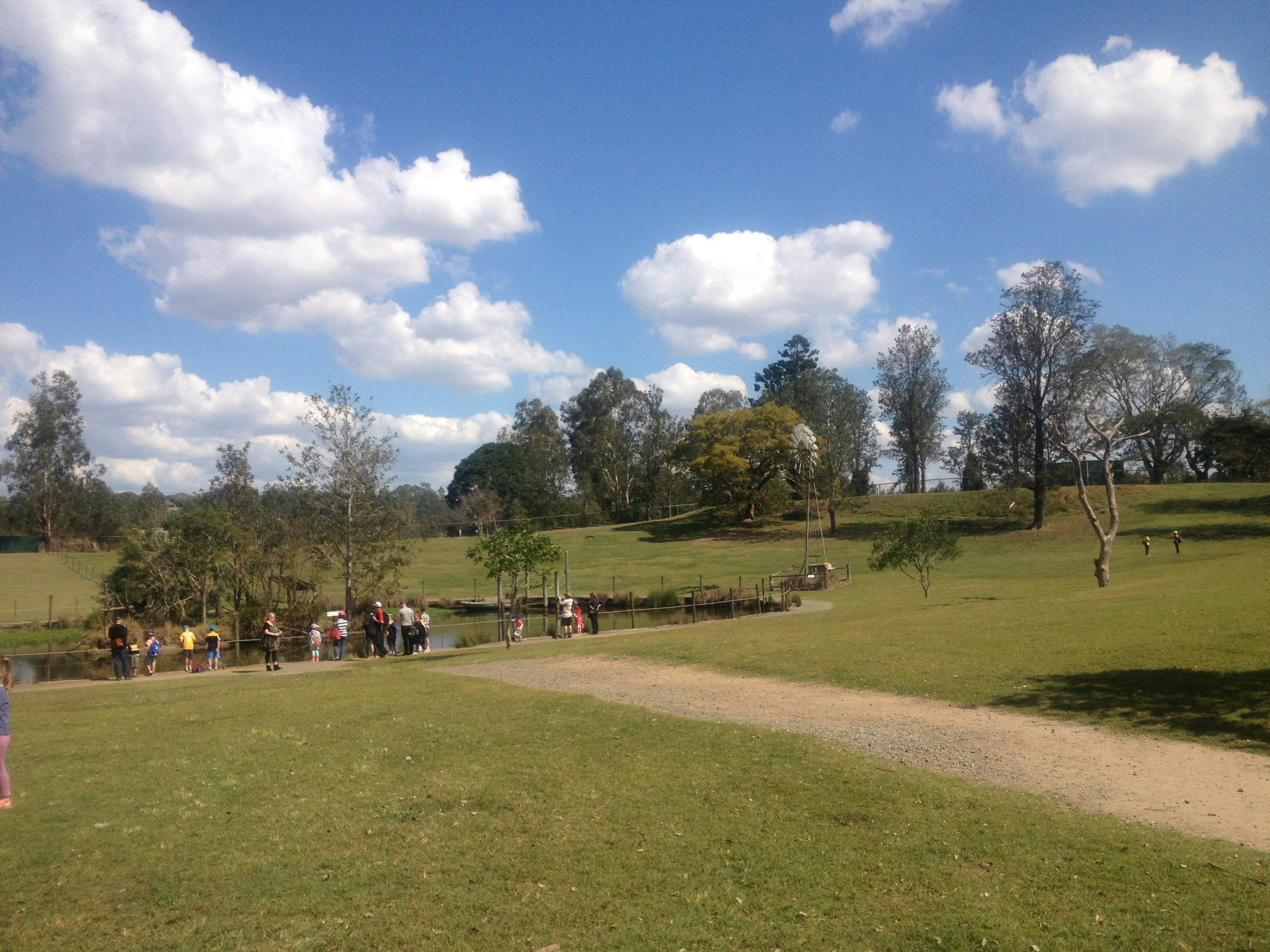 Park scene with blue sky and white clouds people gathering on a path and green grass