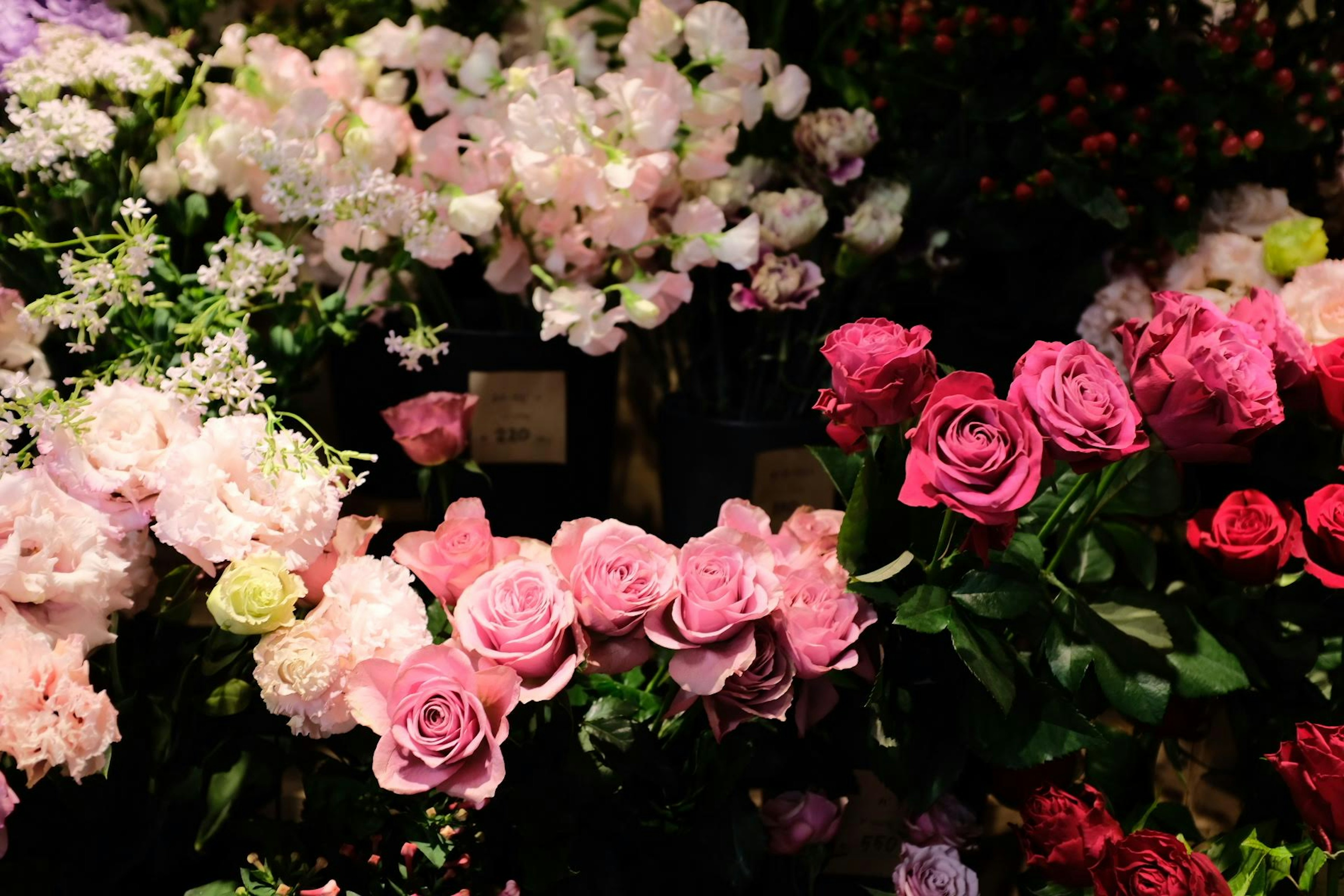 A vibrant flower shop display featuring pink roses and various other flowers arranged beautifully